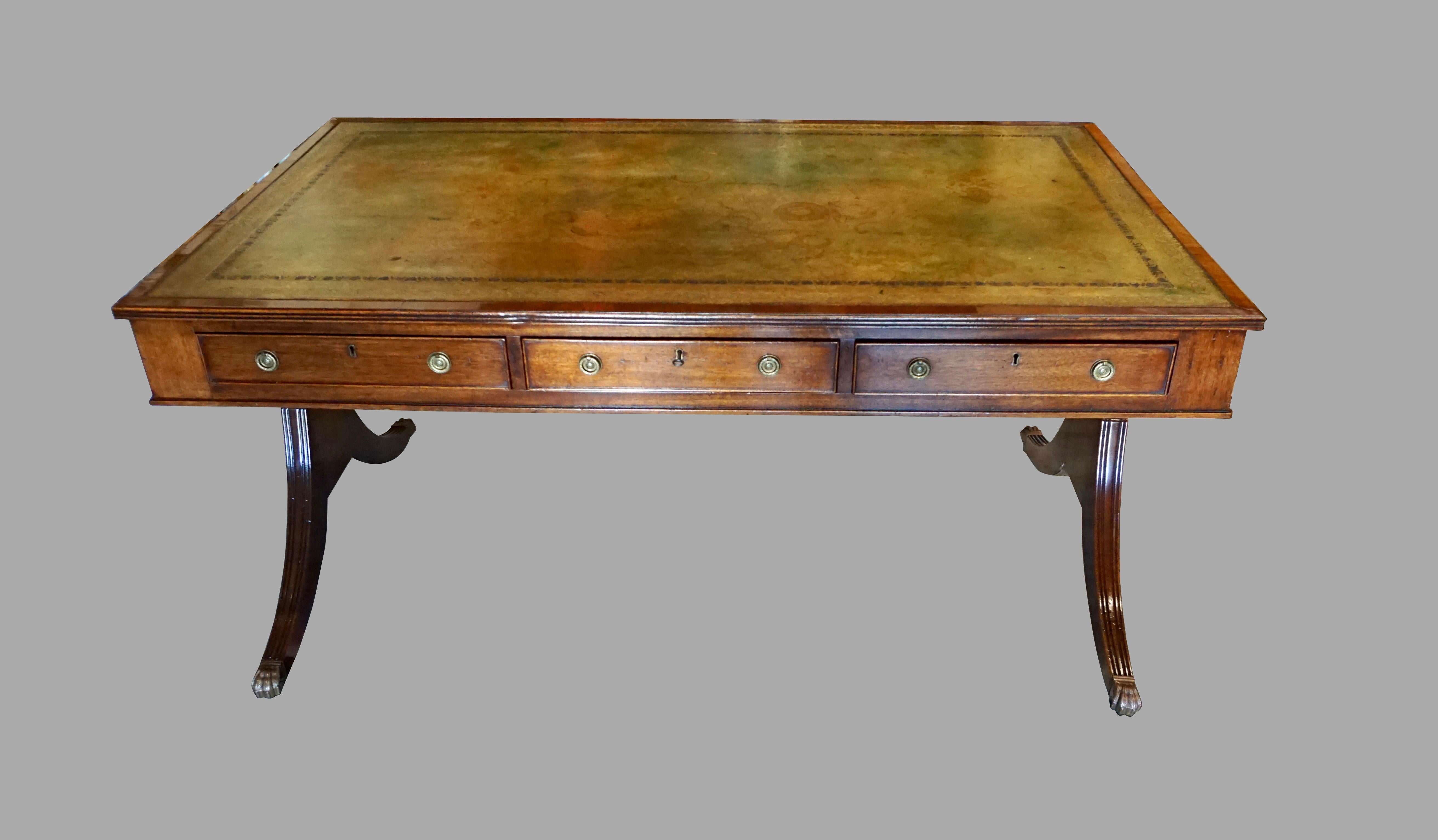 A handsome English Regency style mahogany writing table with a gilt-tooled tobacco colored leather top. The front has 3 functioning drawers and the back has 3 matching dummy drawers. The piece is supported on reeded downswept legs joined by a high