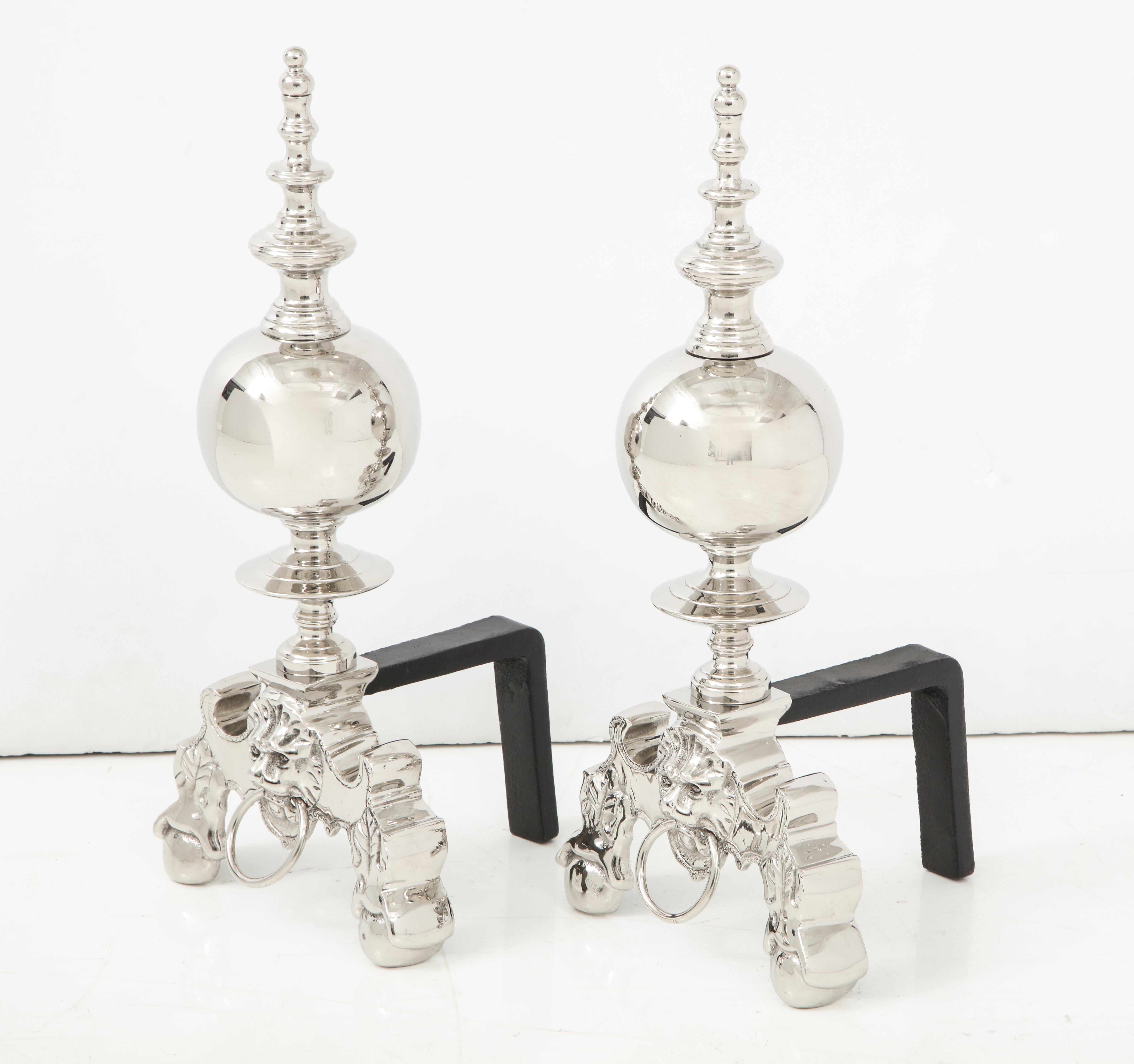 Pair of stylish polished nickel andirons with lion's head with ring front details and tapering spire with blackened iron backs. Professionally polished.
