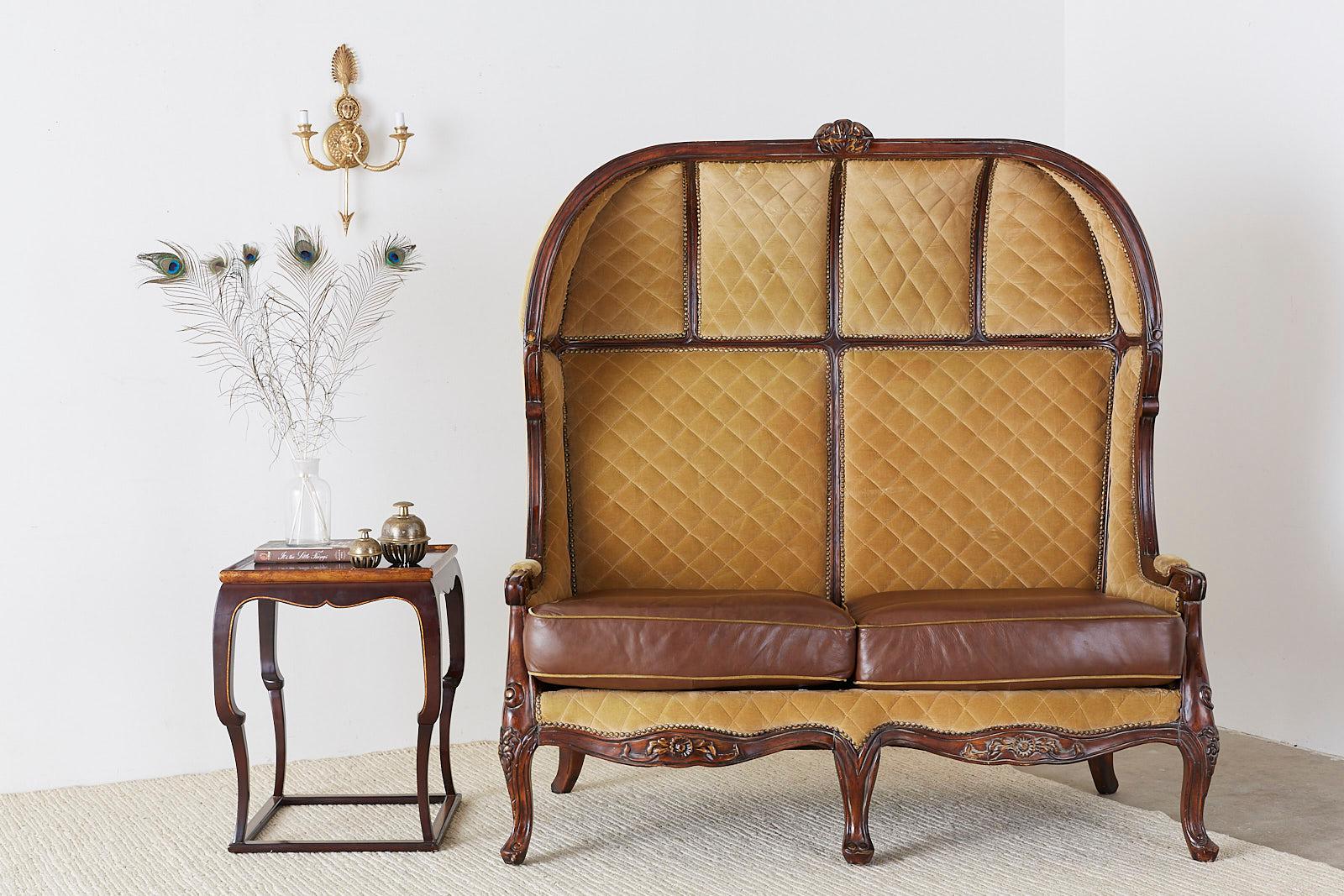 impressive porter's settee or canopy settee constructed from mahogany in the English regency taste. Features a beautifully hand carved hooded frame upholstered with quilted velvet bordered by fancy brass tack nail head trim. The seat is fitted with