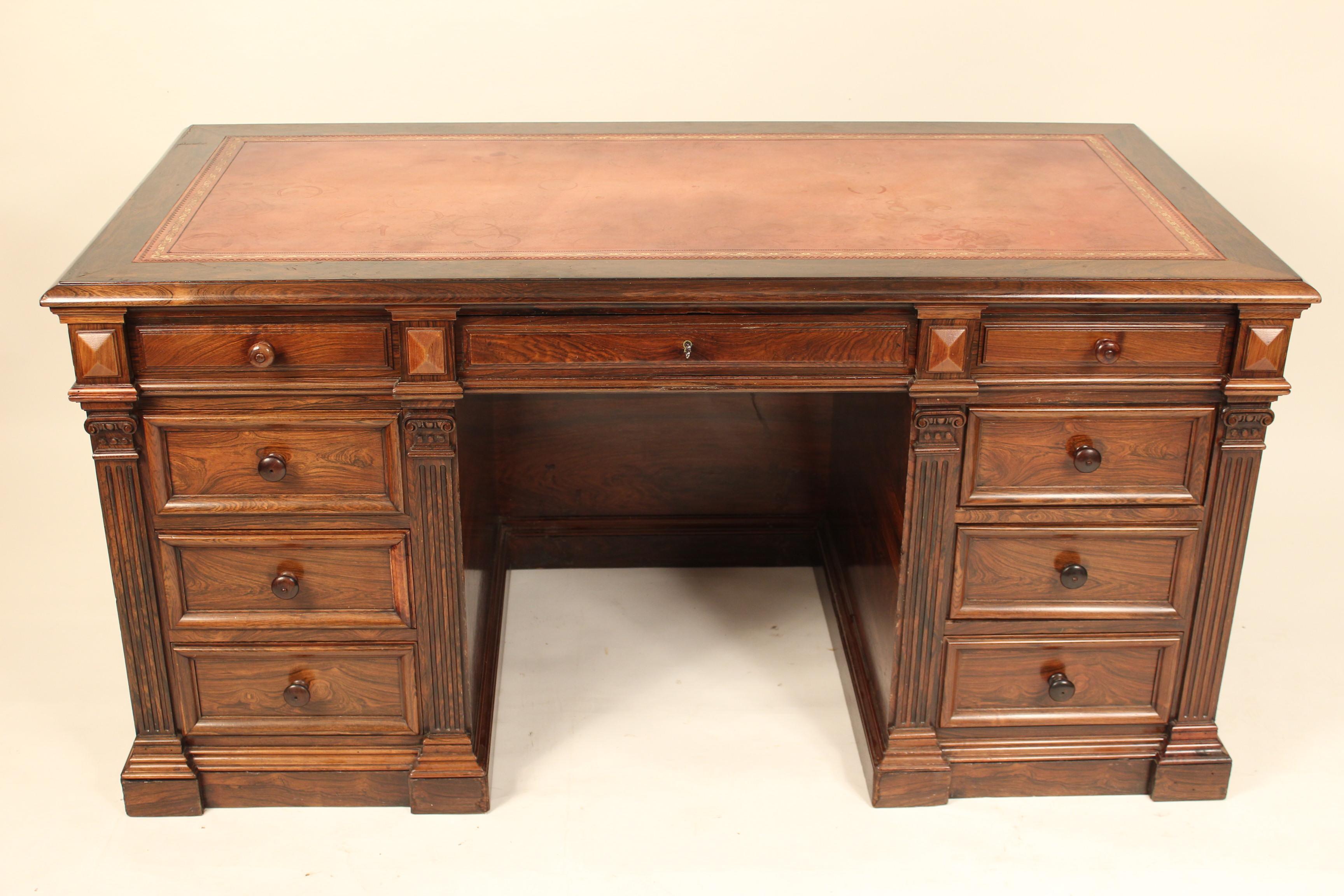 English Regency style rosewood desk with leather top, circa 1920. There are writing slides with leather tops that pull out / pull-out from each end. This desk has a locking mechanism, when the center drawer is closed or locked the side drawers are
