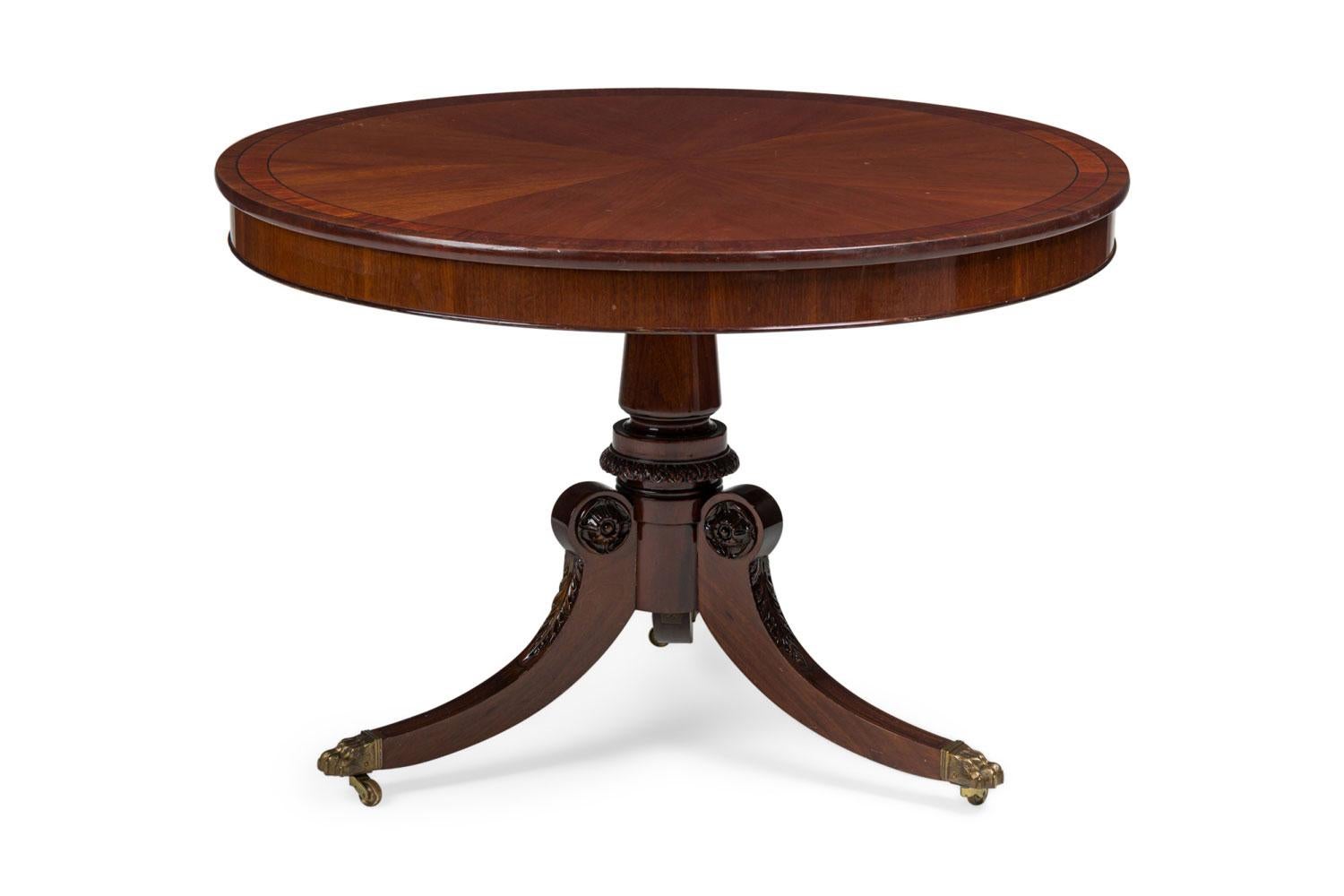 English Regency style (late 20th Century) mahogany round center table with black inlay on the top and a carved pedestal base ending with three brass sabots with casters