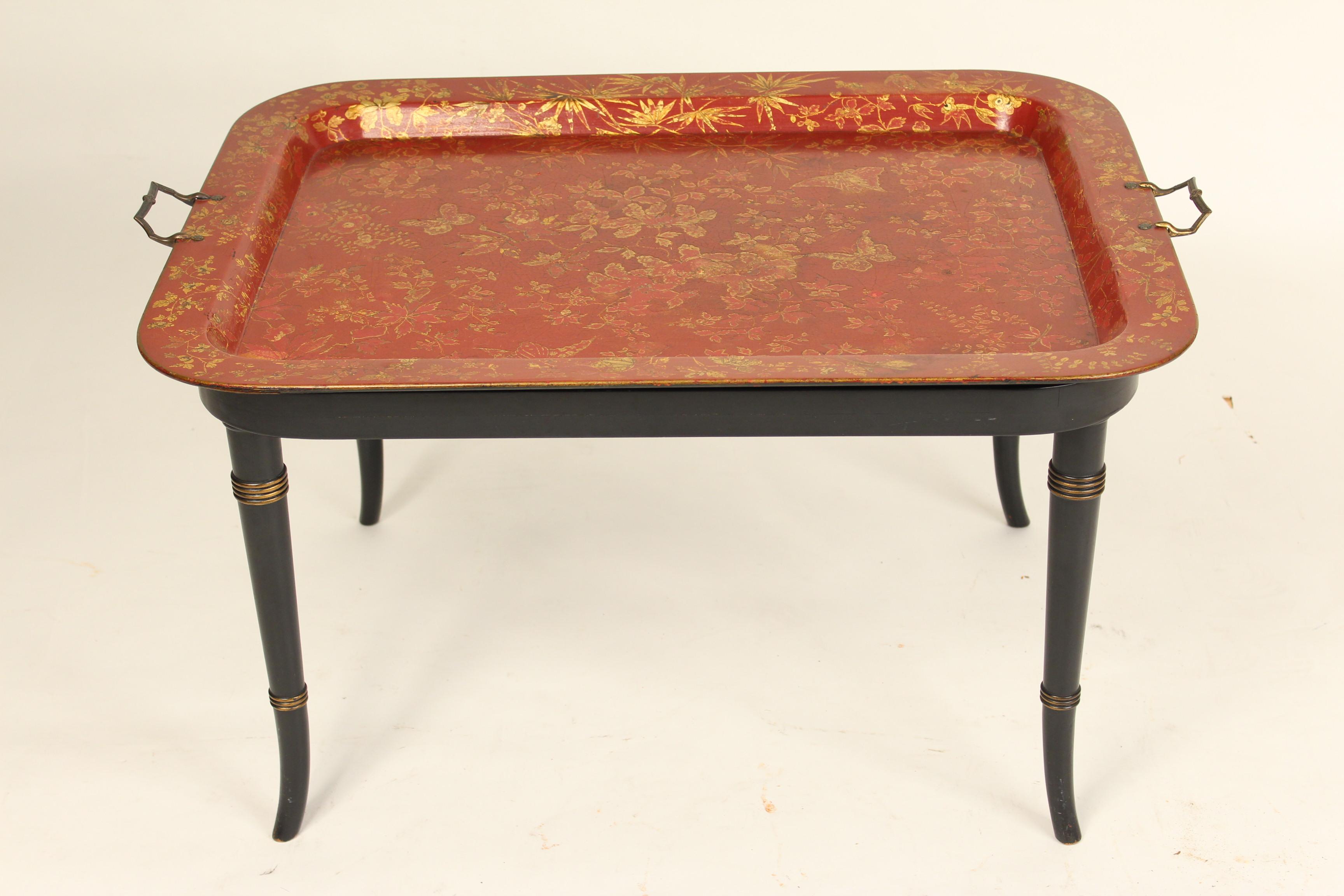 English Regency style red papier mâché and gilt decorated tray with brass handles, late 19th century, resting on a 20th century stand. The bottom of the papier mâché tray is marked 