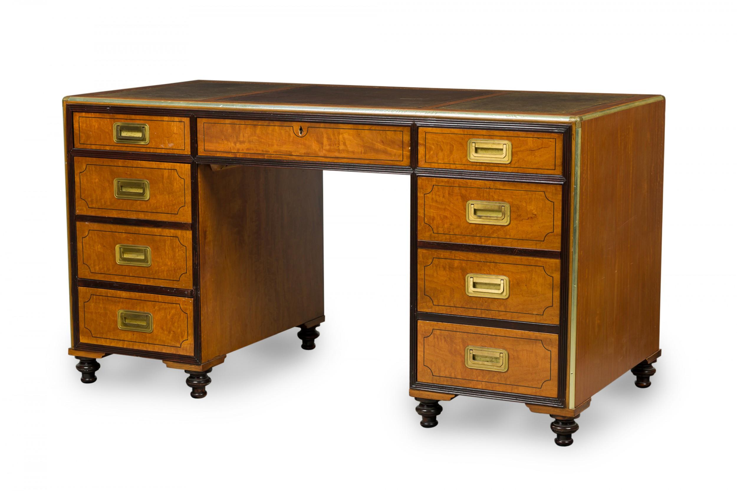 English Regency-Style (20th century) Campaign / kneehole desk with two cabinet columns with four drawers each having square inset brass drawer pulls and ebonized trim, and a central drawer, supporting a desktop with three brown leather insets.