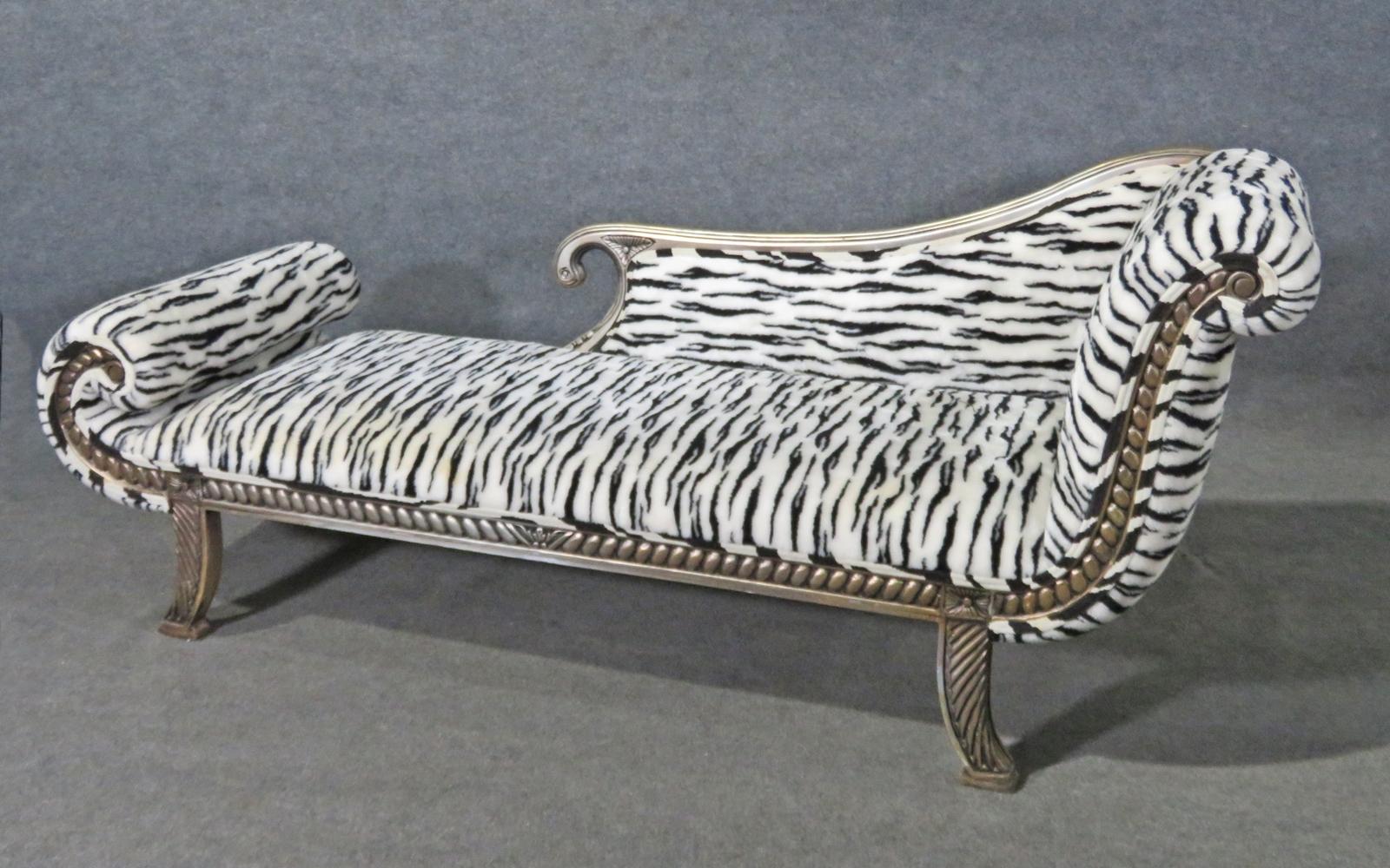 This is a very unique and eye-popping chaise or recamier. The piece is designed in a stylized English Regency style. The upholstery is a furry zerba print and in decent condition. The dimensions are 35 1/2