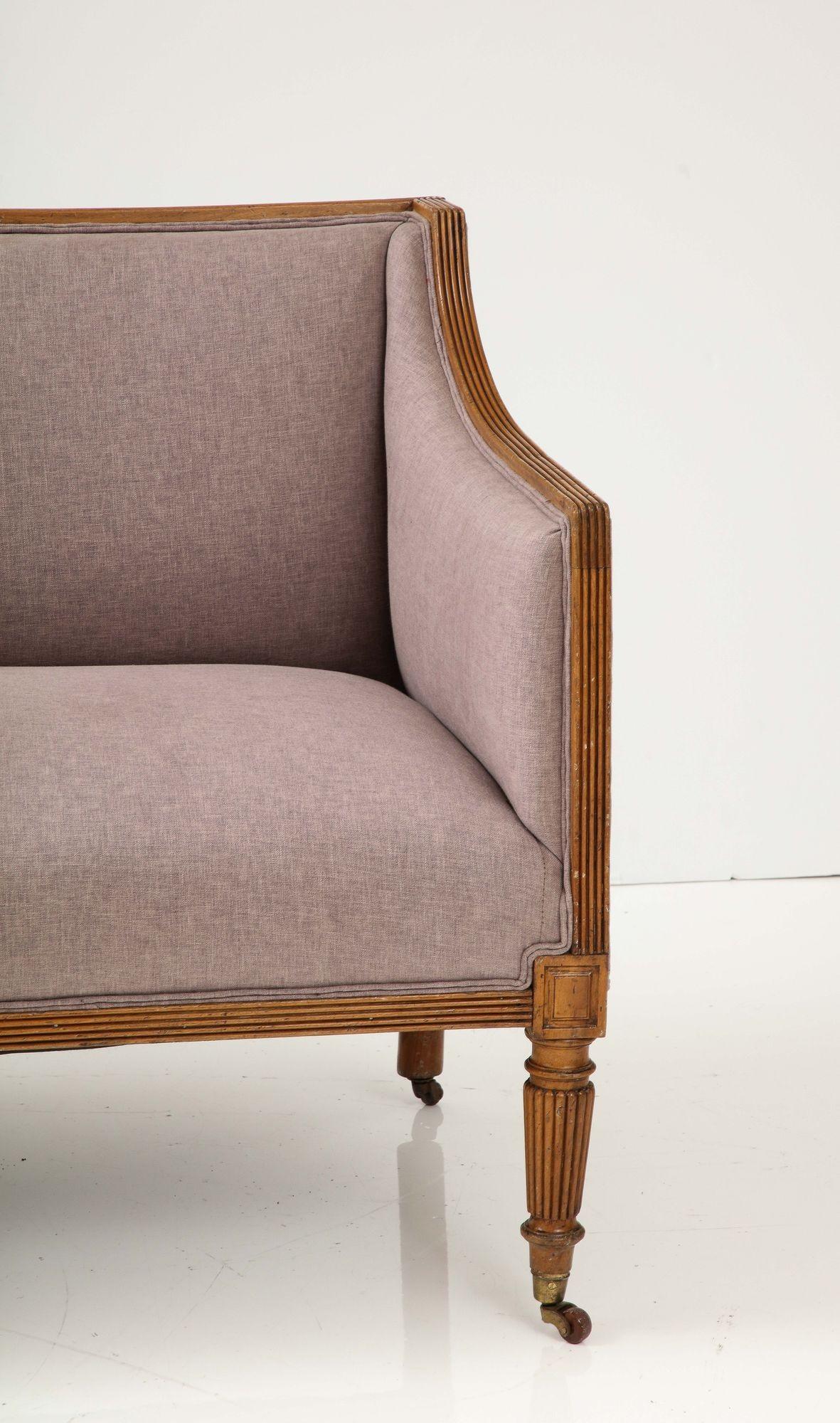 Experience the elegance of the English Regency era with this exquisite early 19th-century fruitwood square back loveseat. Adorned with classical sloping arms and a meticulously crafted reeded wood frame, it encapsulates the timeless charm of the
