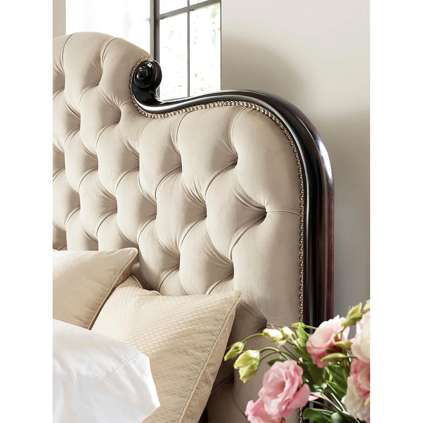 A fine English Regency style carved and upholstered queen-size bed. With carved serpentine top rails and a button-tufted and upholstered headboard and footboard. 

A beautiful blend of dark wood, intricately carved scrolls, and lush fabrics.