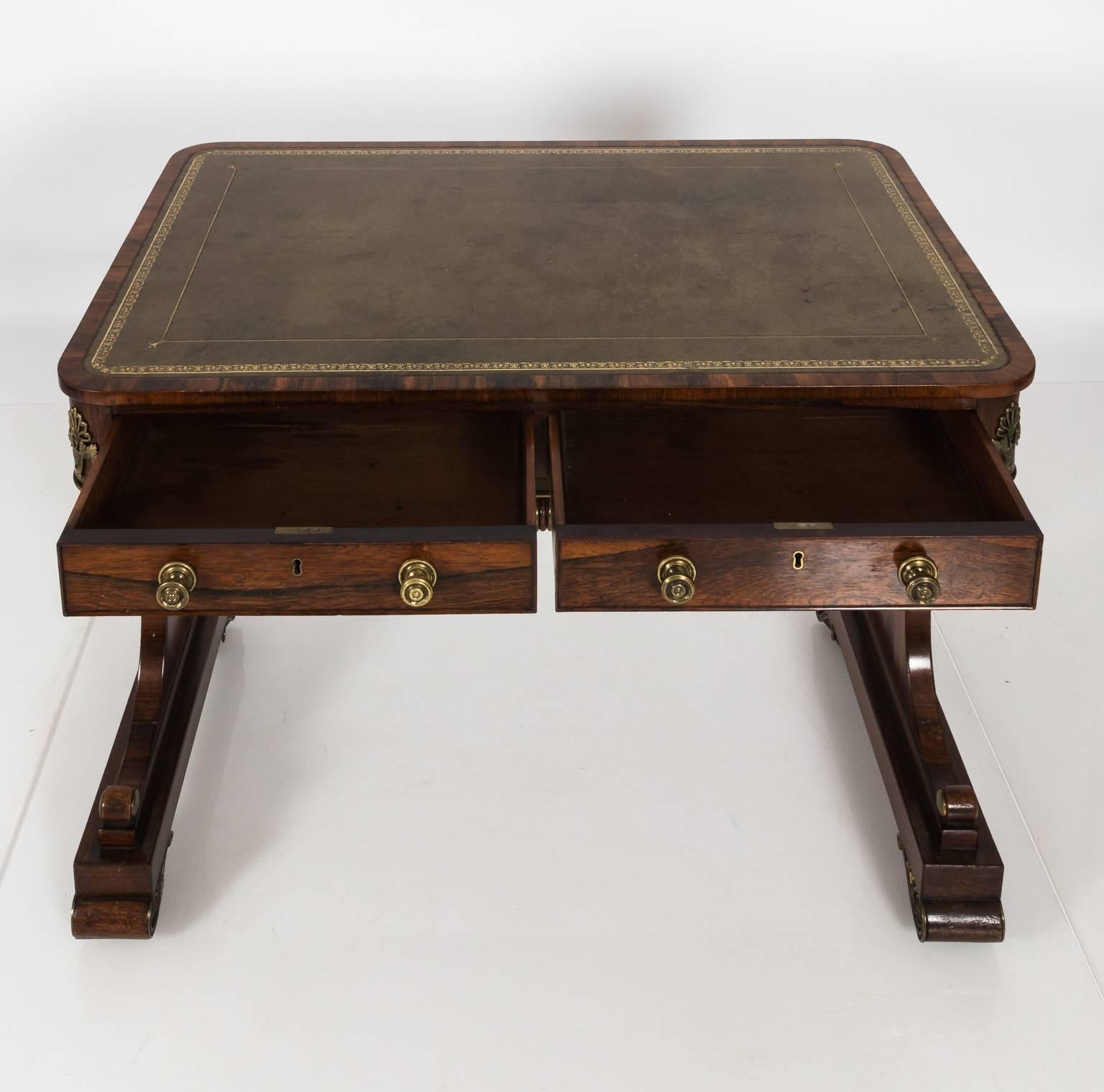 English Regency style two-drawer rosewood writing table from an estate in Hyde Park, NY that features a leather embossed tabletop with some minor staining and scratches, circa 1820. This table also features a trestle base with decorative brass trim