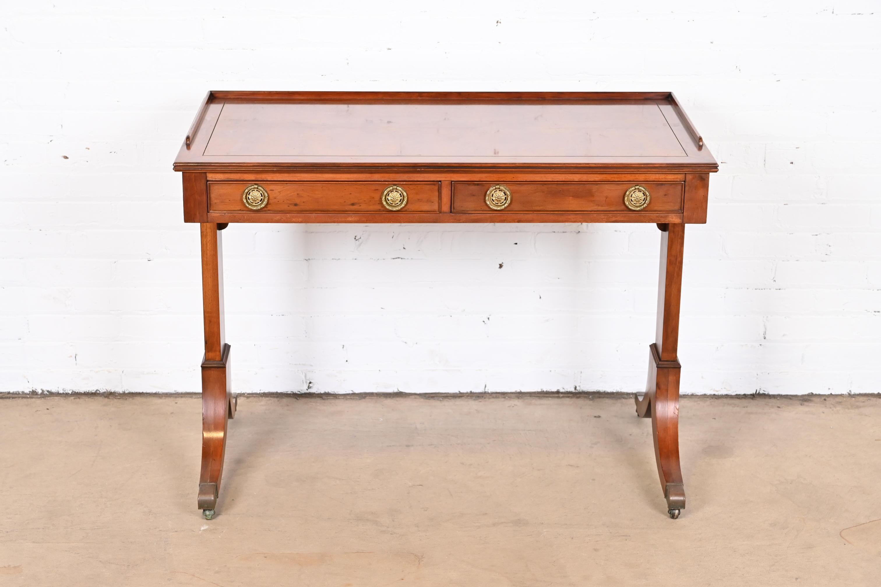 A gorgeous English Regency style writing desk or console table

In the manner of Baker Furniture

Mid-20th Century

Yew wood, with original brass hardware and brass-capped feet.

Measures: 40