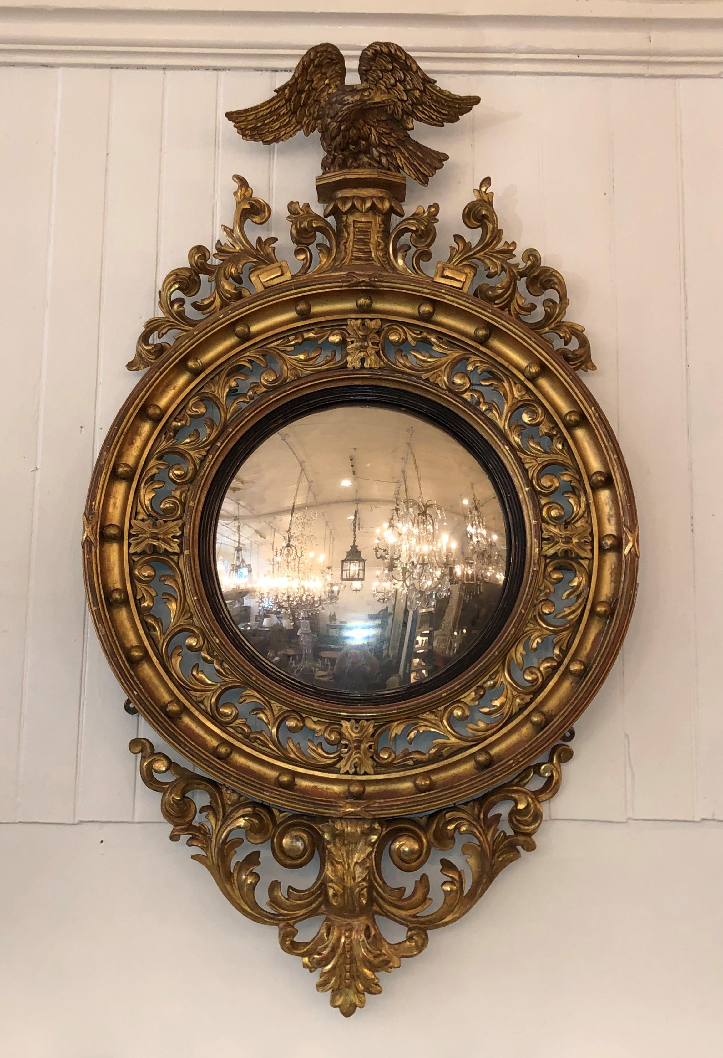 This imposing Regency convex mirror is hand carved and gilded. The pediment has an eagle perched on a plinth flanked by foliage scrolls. The mirror frame is opened pierced craved with foliage scrolls and surrounded by twenty-four gilded balls. The