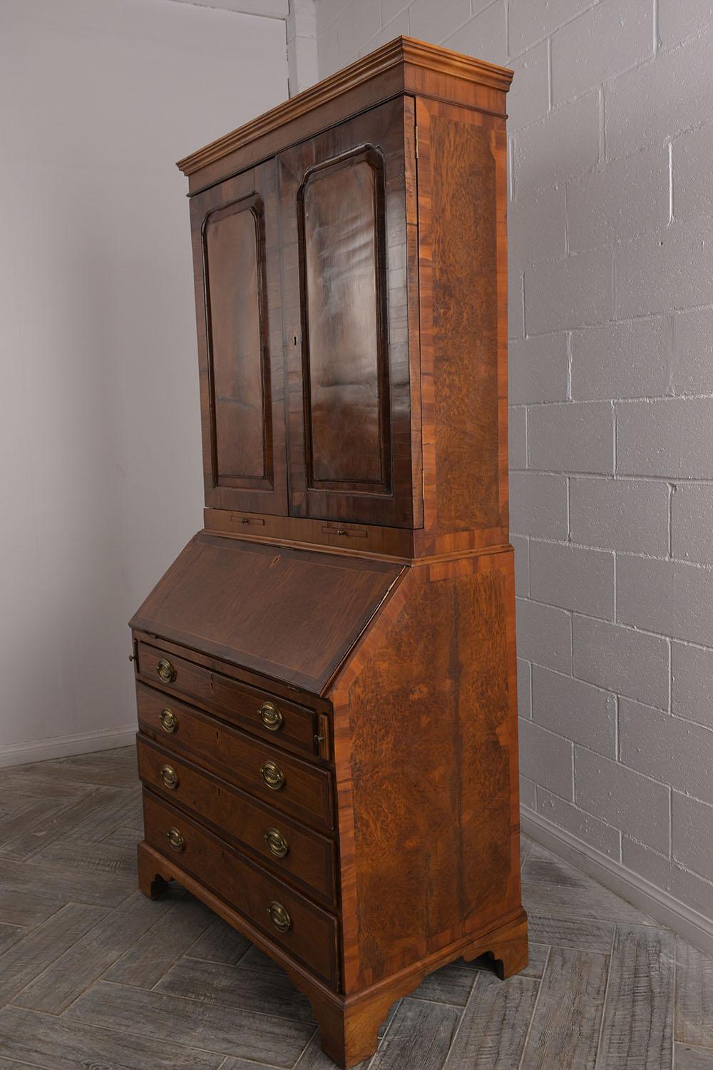 This is an English George III drop front secretaire circa the 1830s. The cabinet top features multiple open shelves small door in the middle along 3 small drawers. The drop deck door has a leather top multiple small storage spaces, drawers, and an