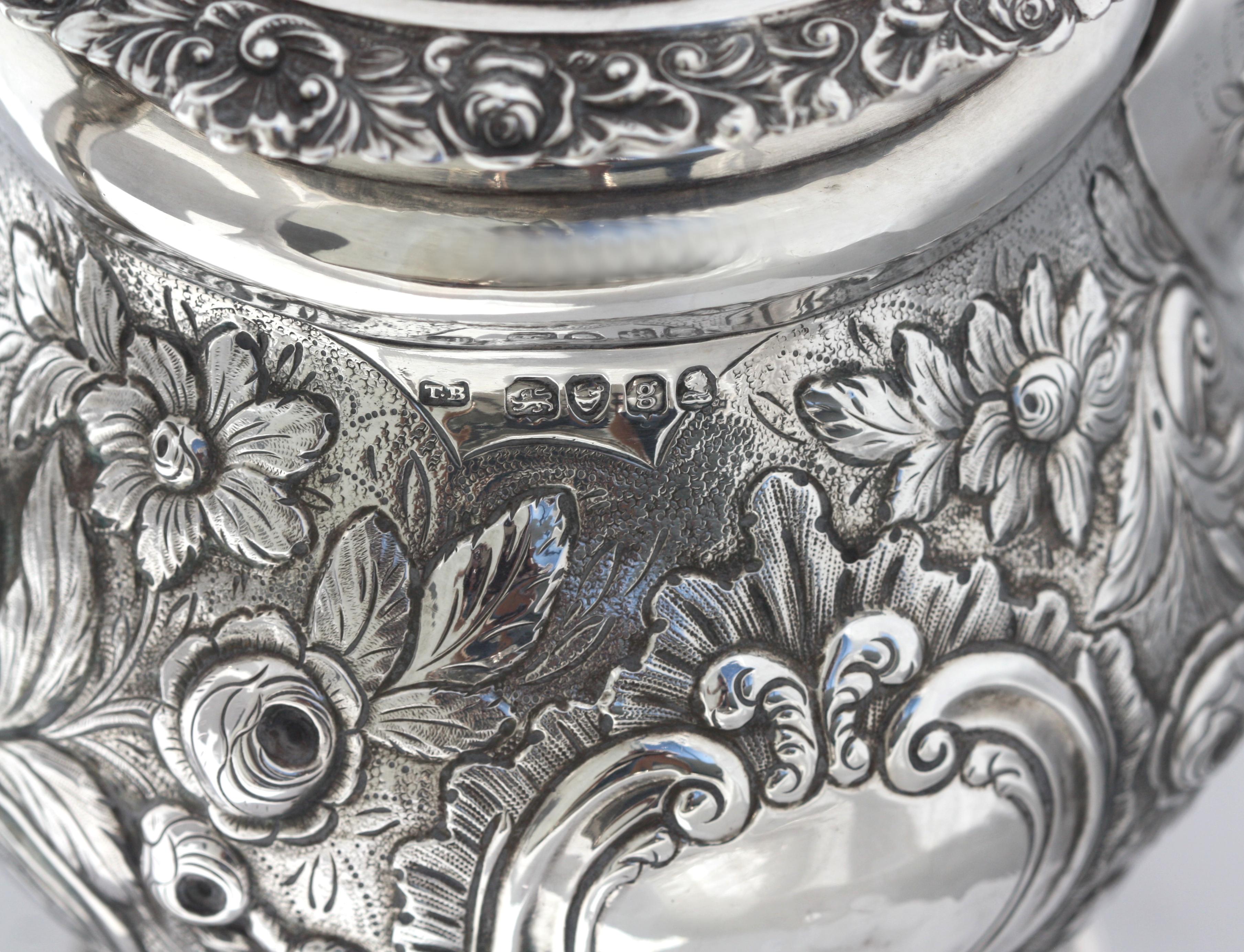 
English Rococo Silver Teapot, Marked, 1822-1823, maker TB, for Thomas Baker, incised on the underside 1695976. The body, hinged lid, lid and circular foot chased all over with foliage and with two cartouches, with a scrolled leaf-cast handle and