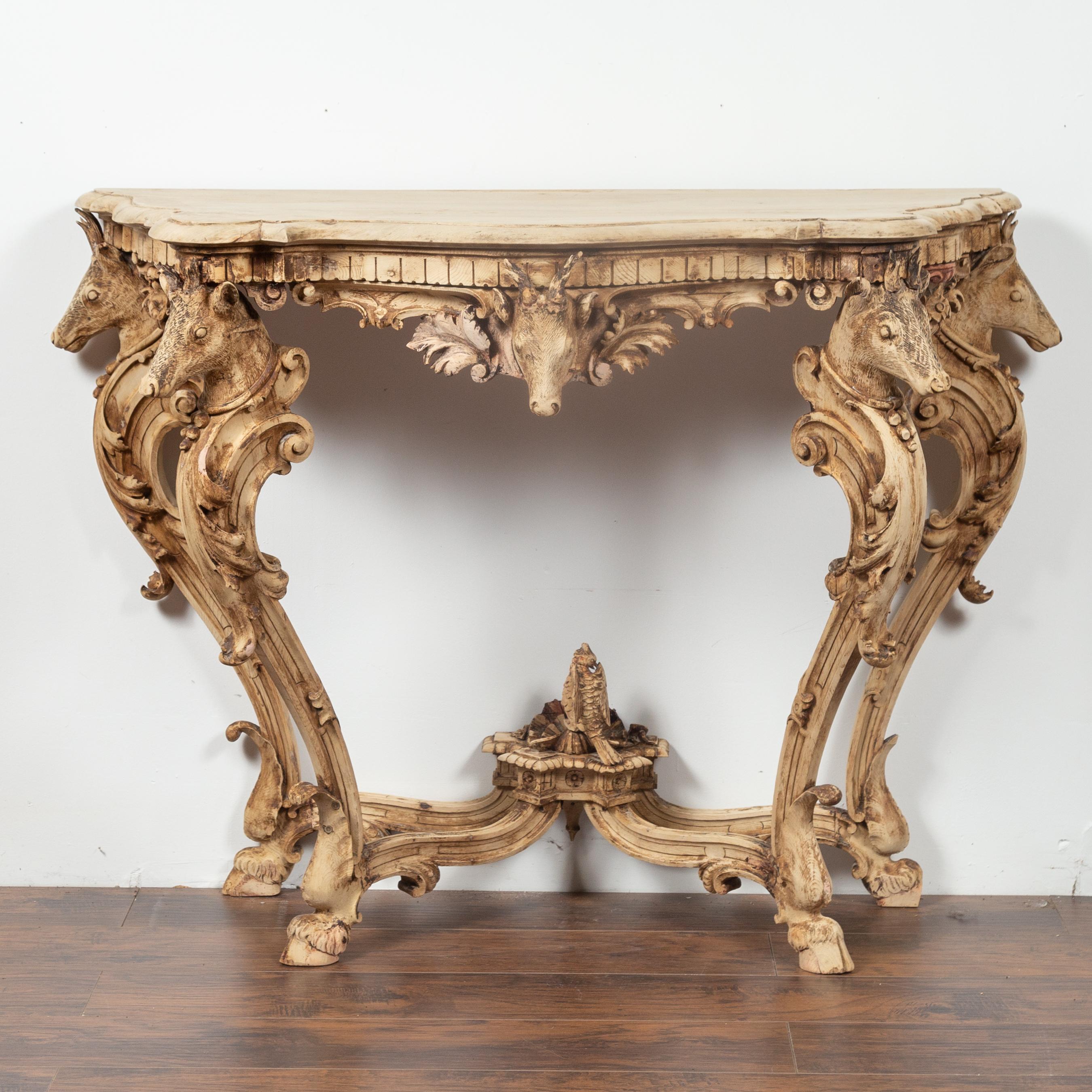 An English Rococo style carved and bleached oak console table with deer heads and hoofed legs from the late 19th century. This English console table features a nicely shaped planked top with beveled edges, sitting above an exquisite Rococo style