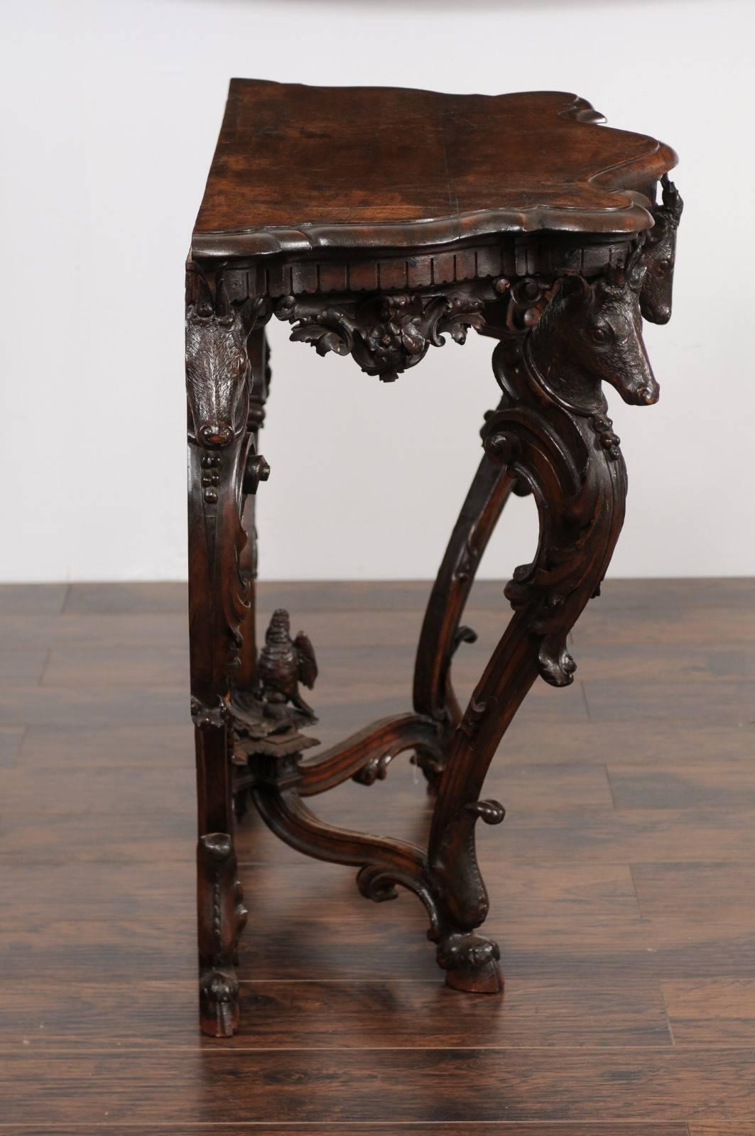 An English Rococo style richly carved oak console table with deer heads and hoofed legs from the late 19th century. This English console table features a nicely shaped planked top with beveled edges, sitting above an exquisite Rococo style base,