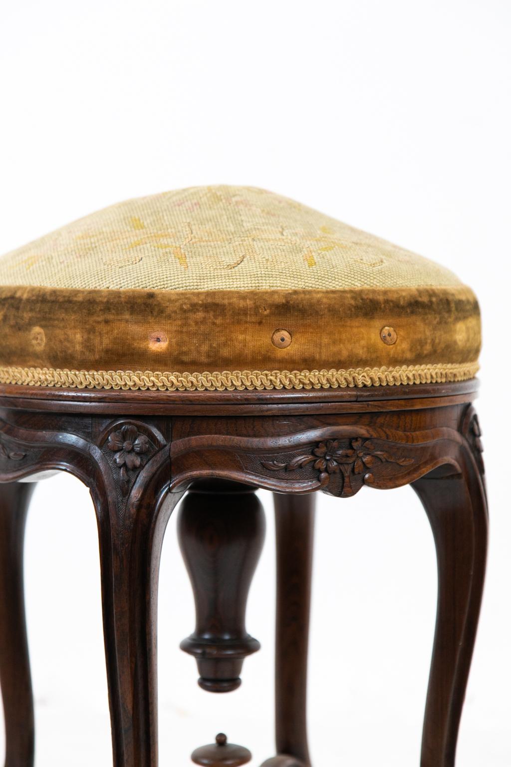 English rosewood cross stretcher stool, has carved rosettes and scroll work joined by two turned carved scroll shaped cross stretchers. The center joint of the stretchers has a turned finial. The needlepoint seat is floral with stitched initials.
  