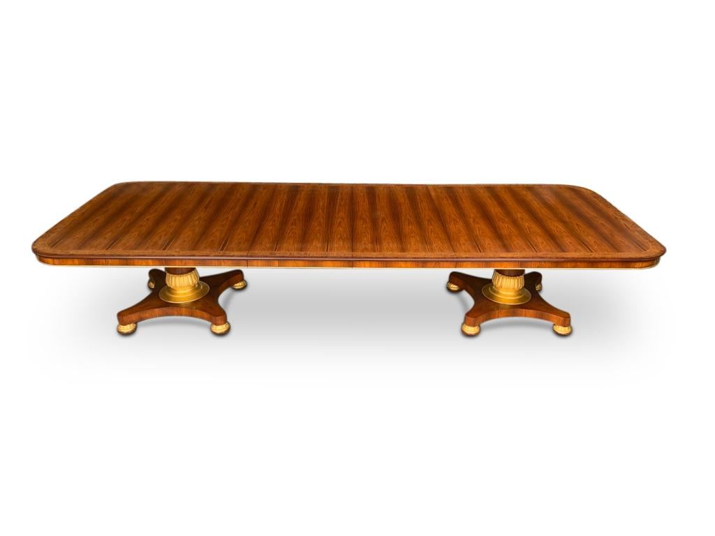 An English rosewood dining table, 20th century. This magnificent Regency style two pedestal two leaf rosewood dining table rests on four sided platform bases. The pillar and turned bun style feet have hand carved leaf decoration finished in oil