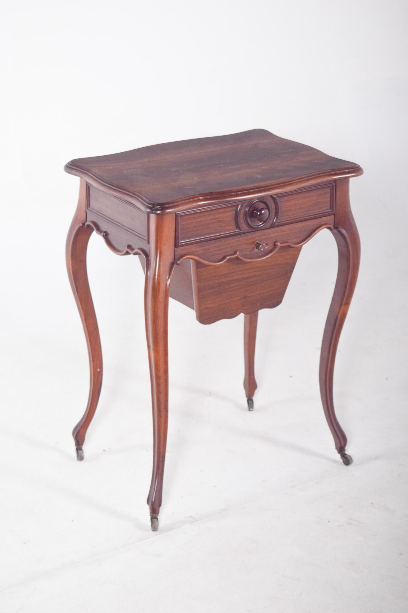 Table de pot en bois de rose. Pieds fortement incurvés, terminés par de petites roues en métal. Le plateau est découpé aux extrémités, avec un contour ondulé, et la façade comporte un faux tiroir supérieur et une ouverture inférieure en forme de
