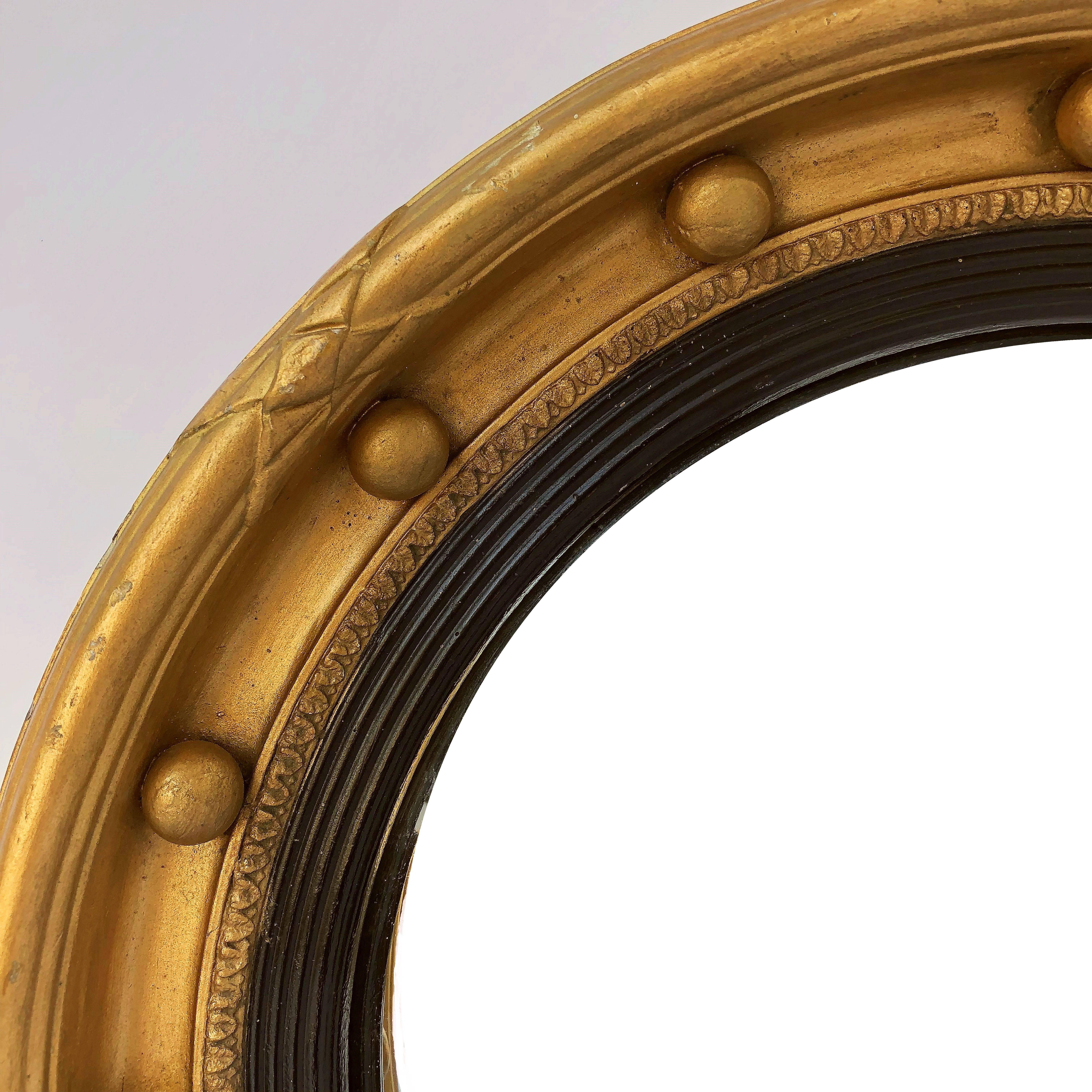 A fine English round convex mirror featuring a Regency design of a moulded gilt and ebonized frame with gilt balls and around the circumference.

Measure: Diameter is 18 1/2 inches
Depth 2 1/4