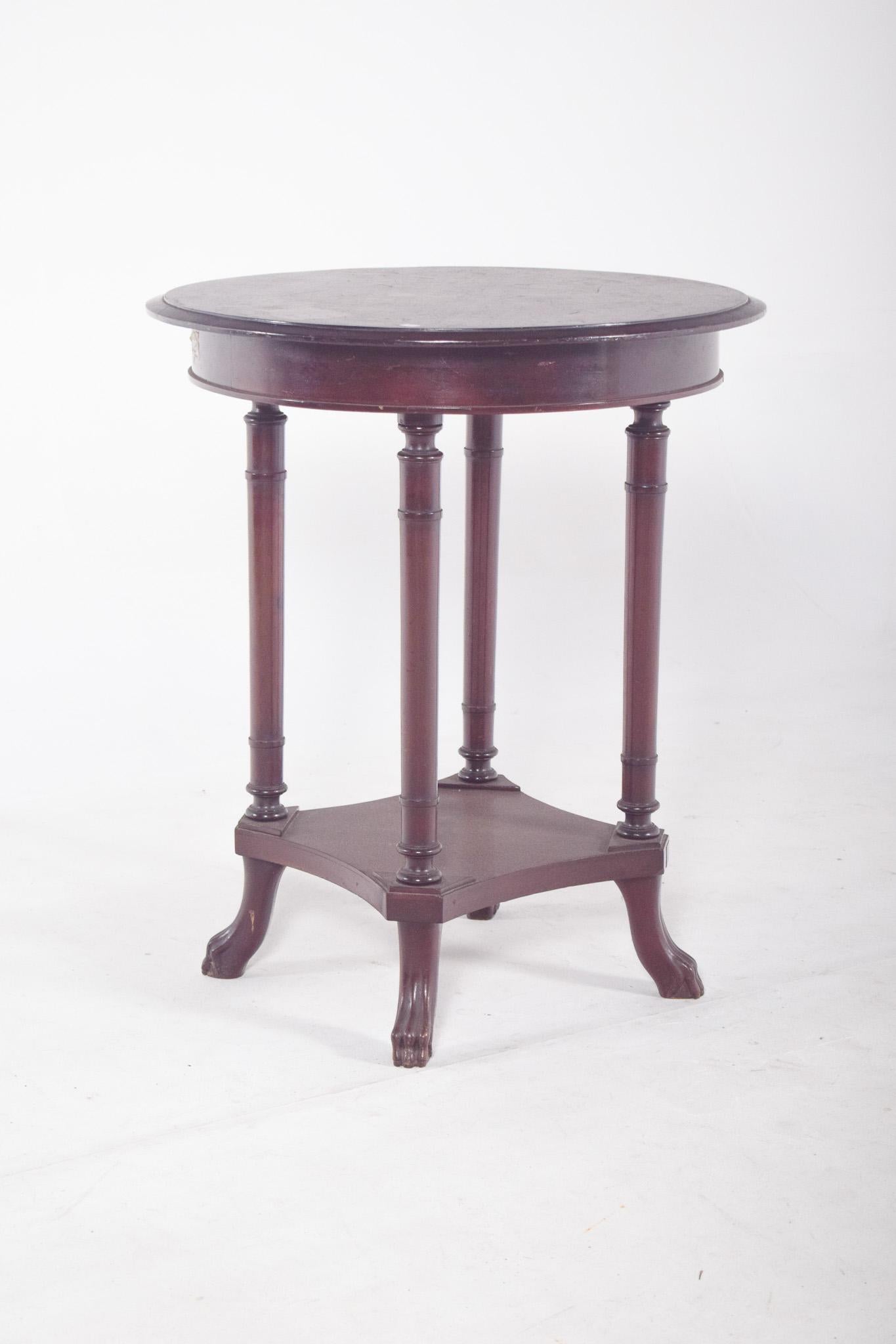 Round coffee table. With a smooth top, resting on four elegant turned legs connected to each other by a bottom rail in a square tray with curved corners. Each leg ends in a sculpted claw, suggesting the influence of the Empire style or neoclassical