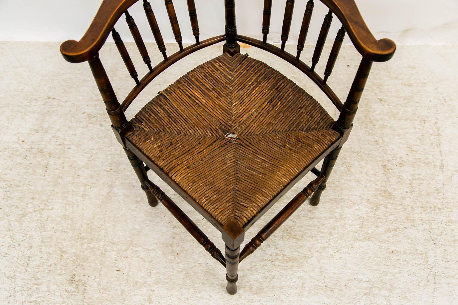 This fruitwood corner chair has a spindle back. The scrolled arms are supported by five turned spindles on each side. The legs are turned and supported by high-low stretchers. The rush seat is missing several strands of rush in the center but is