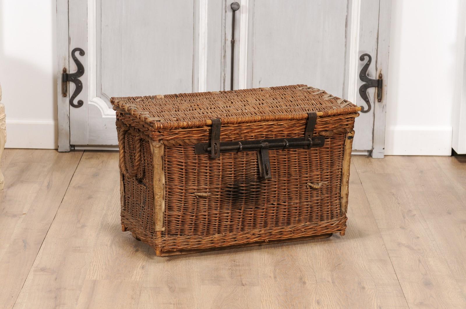 An English rustic wicker trunk from circa 1930 with iron hardware, rectangular lid, lateral handles and fabric lined interior. Capturing the essence of English craftsmanship, this rustic wicker trunk from circa 1930 is an exquisite fusion of form