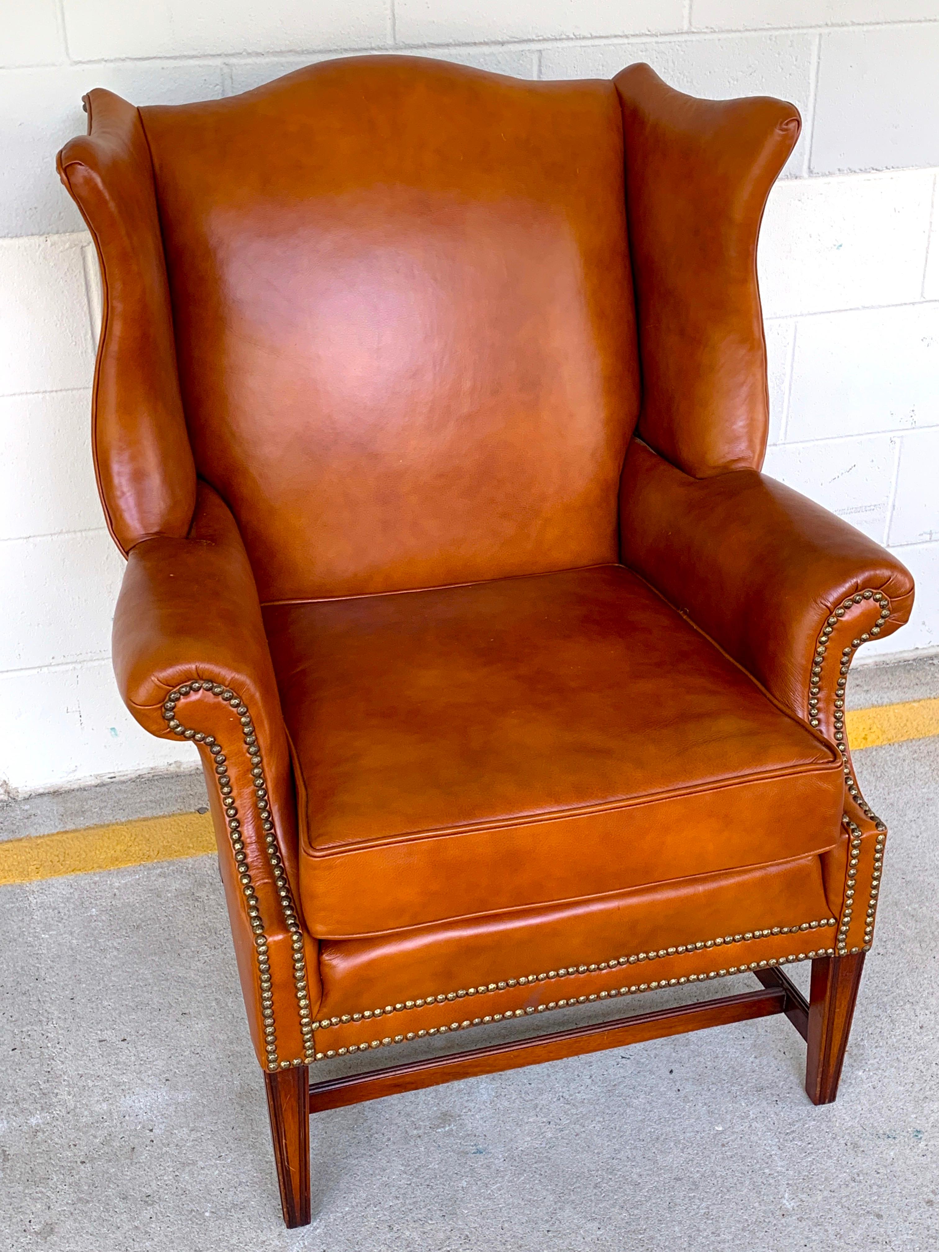 English saddle leather mahogany wingback chair, beautifully shaped lush leather wing chair with brass nailheads, raised on a mahogany stretcher base.
Measures: Arm height 24