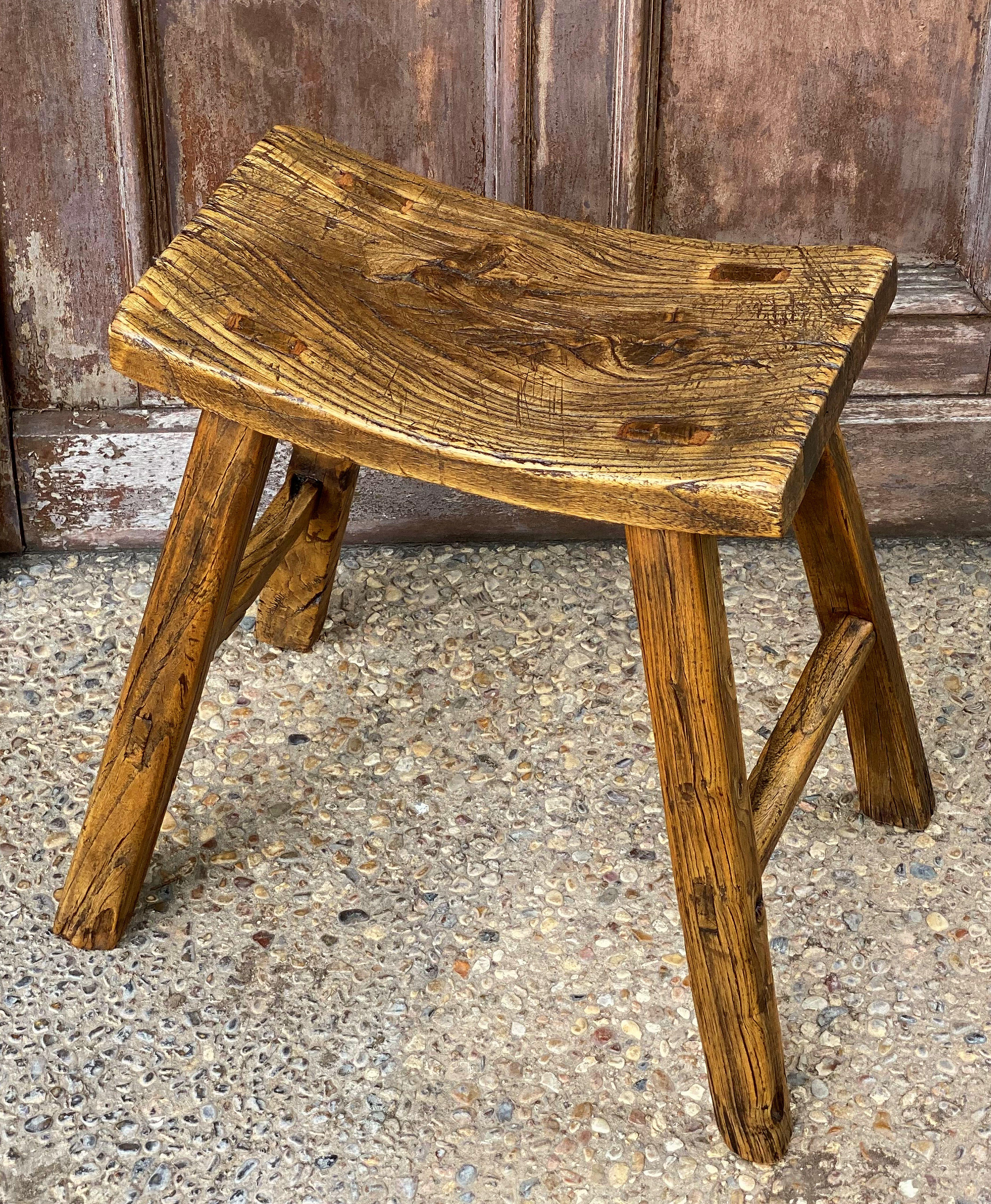 A fine English saddle seat or rustic farm stool of elm, featuring a shaped rectangular seat over four legs.