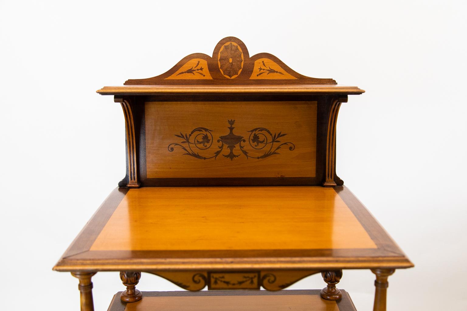 English satinwood cabinet or étagère, with satinwood being the primary wood, and all sides, doors, and shelves are crossbanded with mahogany. The crest, back, aprons, and door are inlaid with mahogany urns and arabesques. The shelf is supported by