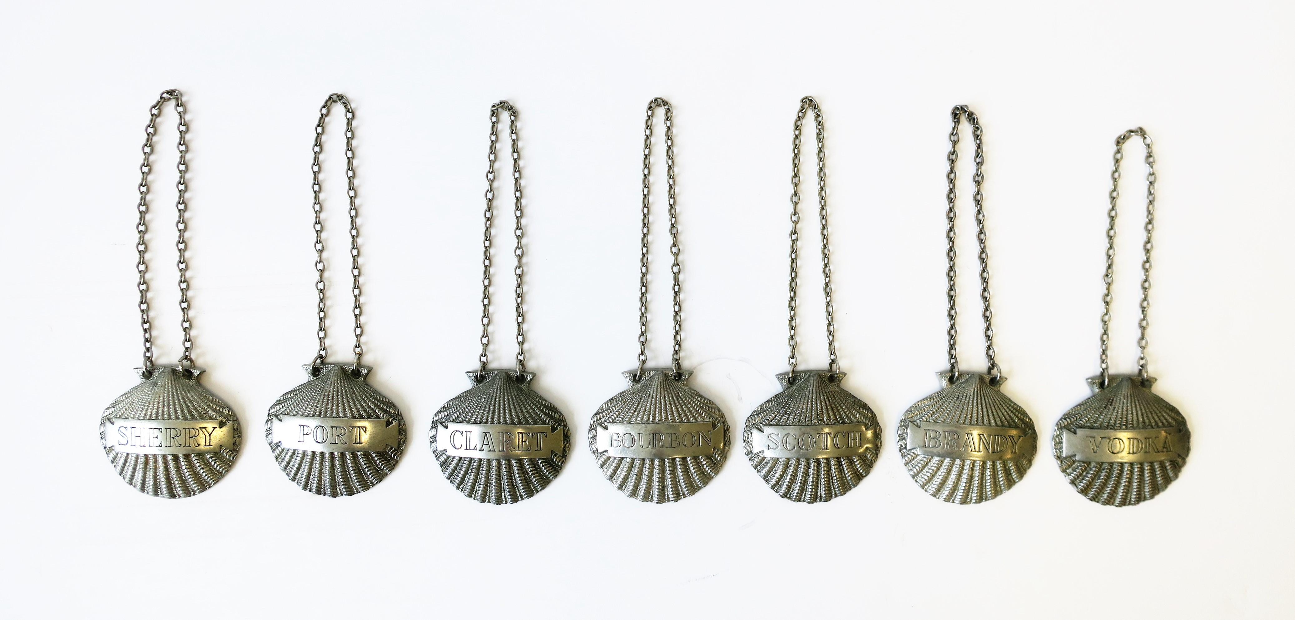 A set of seven (7) English scallop seashell liquor/spirits bottle or decanter bottle tags/labels, circa Mid-20th century, England. Tags are a nice weight with a beautiful detailed scallop seashell design. Tags include the following: Bourbon, Claret,