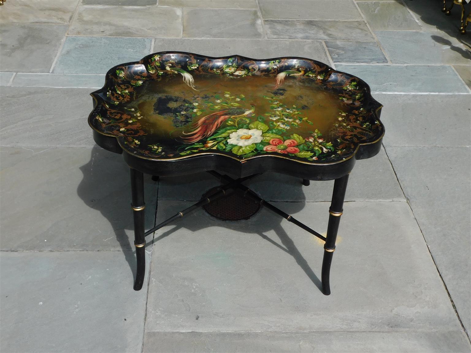 English scalloped Tole tray with decorative Peacock and foliage motif resting on a painted faux bamboo stand with cross stretchers. Early 19th Century.