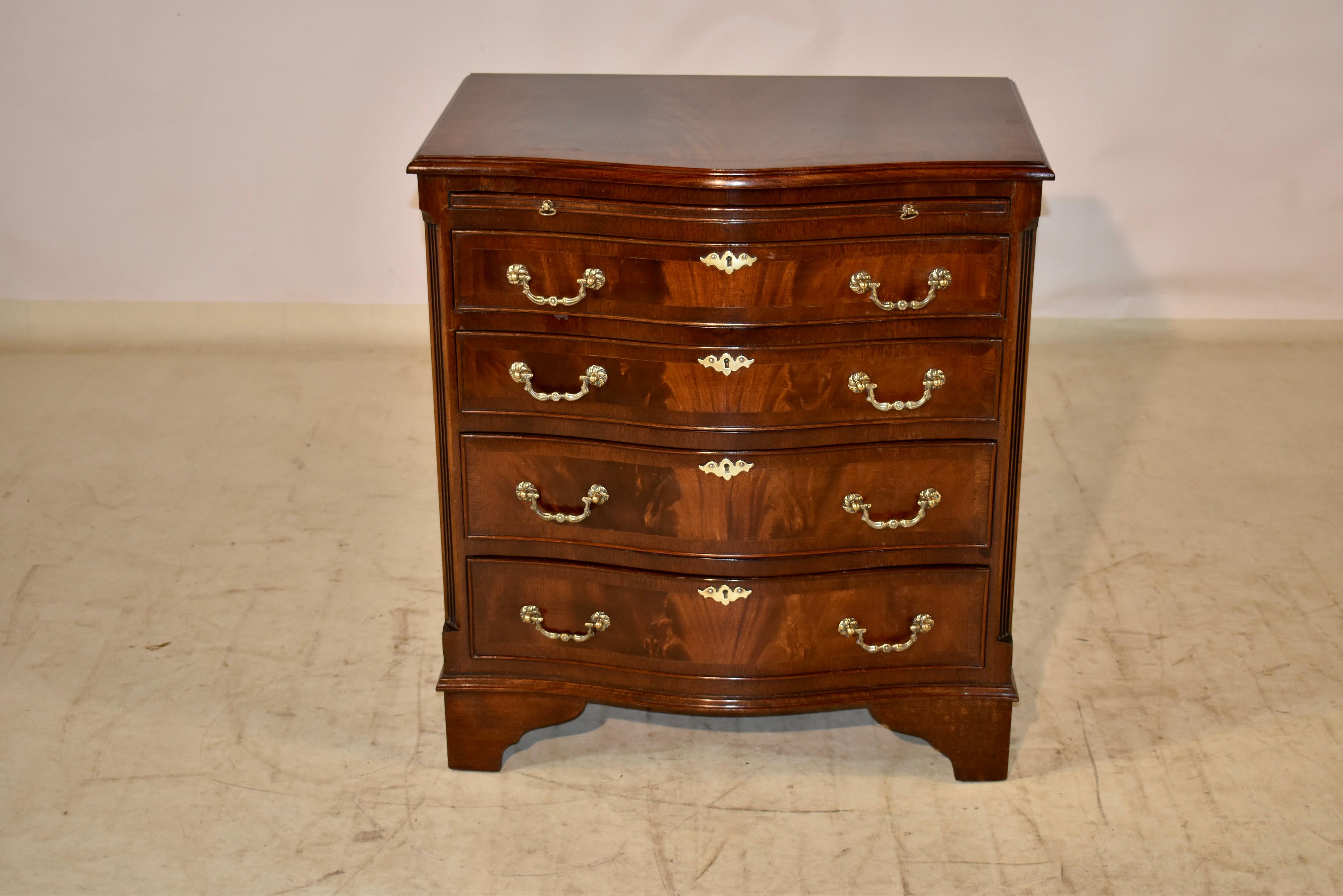 English serpentine side chest made from mahogany, circa 1950. The top is banded in mahogany and has a central panel of flame mahogany with a beveled and serpentined edge, following down to a mahogany slide and four drawers, flanked by fluted quarter