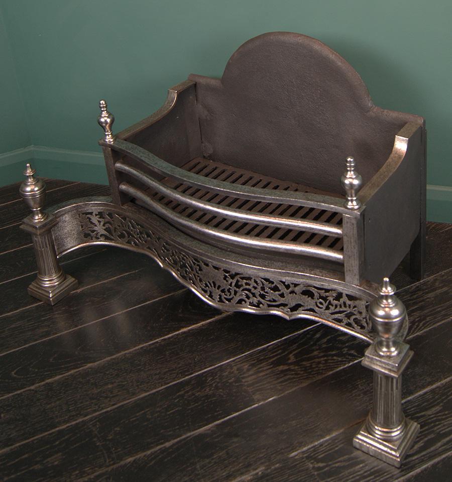 A beautifully proportioned polished steel English serpentine fire grate. The openwork fret with dragon detail is set between Roman Doric column legs on plinth feet, surmounted by urn finials. Shaped arched fire back. A fire grate from the last