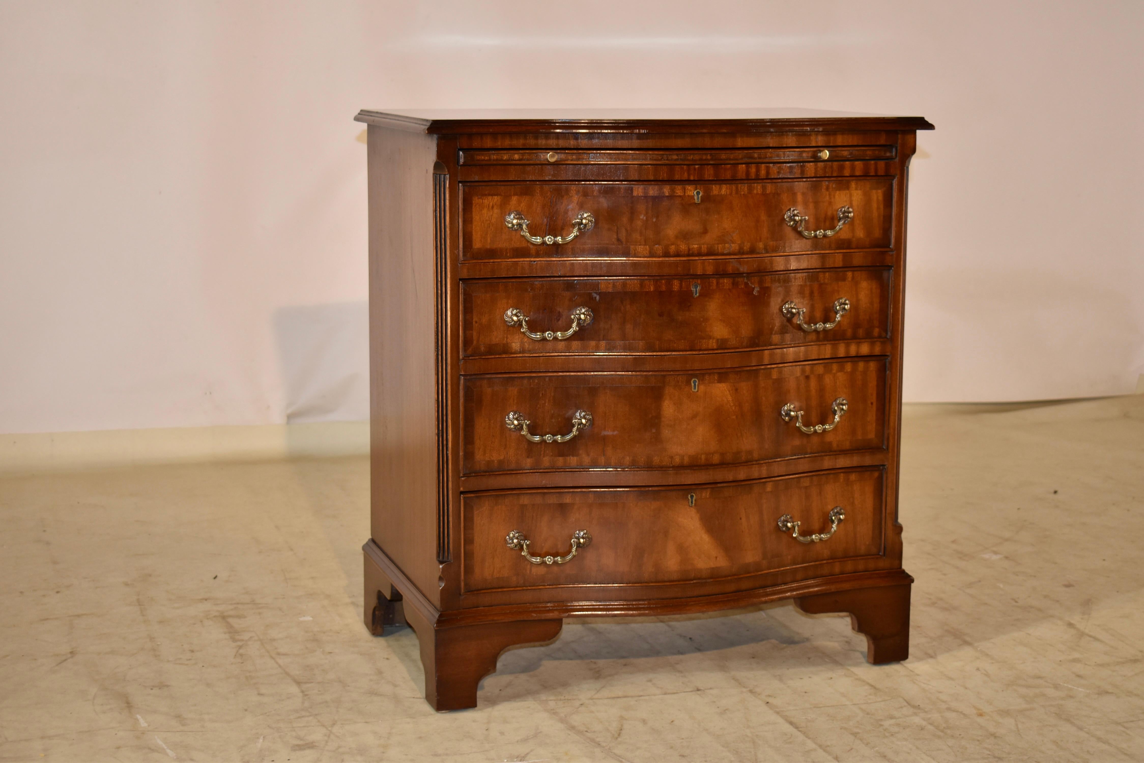 English serpentine side chest from mahogany, circa 1920.  The top is banded in mahogany and has a central panel of flame mahogany with a beveled and serpentined edge, following down to a mahogany slide and four drawers, flanked by fluted quarter