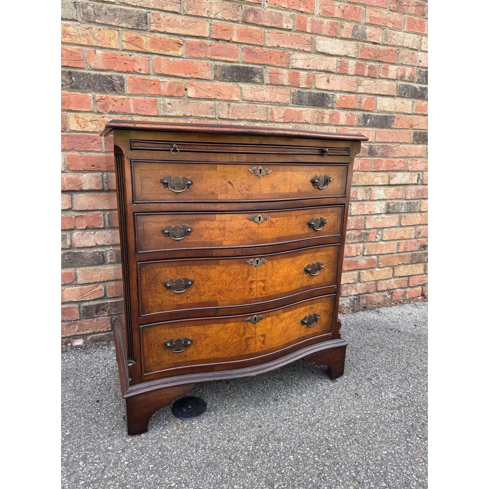 This is Early 20th century serpentine chest of drawers from England and it has a nicely grained top. The is a small chest perfect for an end table are beside a chair has 4 drawers, pull out desk top, and lovely scalloped apron and bracket feet. This