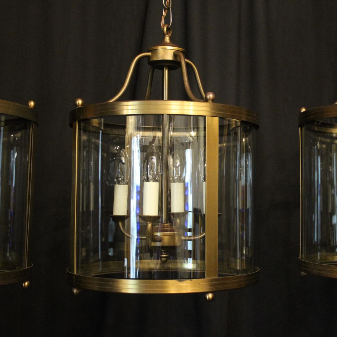 An English set of three 4 light hall lanterns, the 4 scrolling arms with circular bobeche drip pans, surrounded by four sectional circular convex glass panels and held within a simple scrolling framework with open scrolling canopy, having the