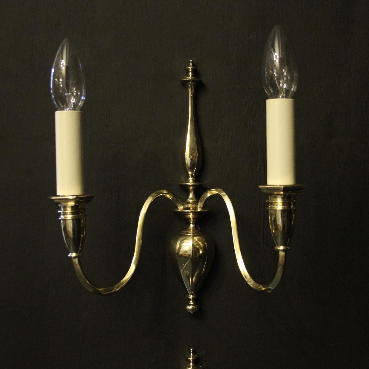 An English set of 4 re-polished cast brass twin arm antique wall lights, the decorative square gauge scrolling arms with hexagonal bulbous candle sconces, issuing from an elongated backplate with sectional bulbous base, sympathetically re-polished