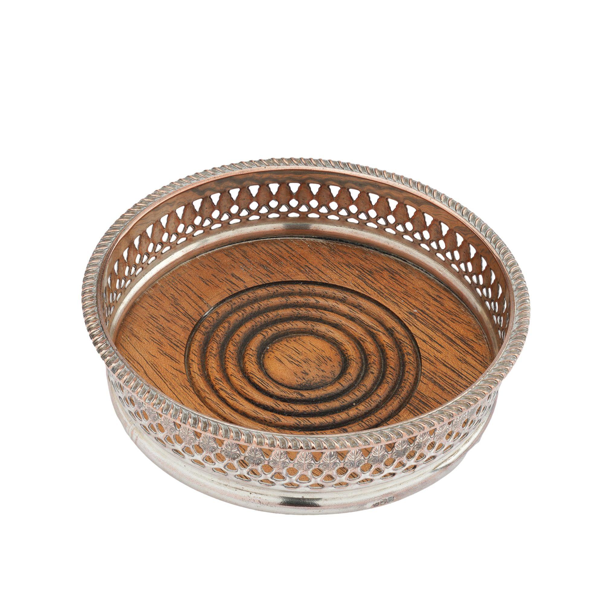 Sterling silver plated copper Sheffield decanter coaster. The coaster is stamped with a Neoclassic anthemion decoration on the pierced gallery below a gadroon molding. A turned wood base is fitted to the bottom of the coaster. A set of three
