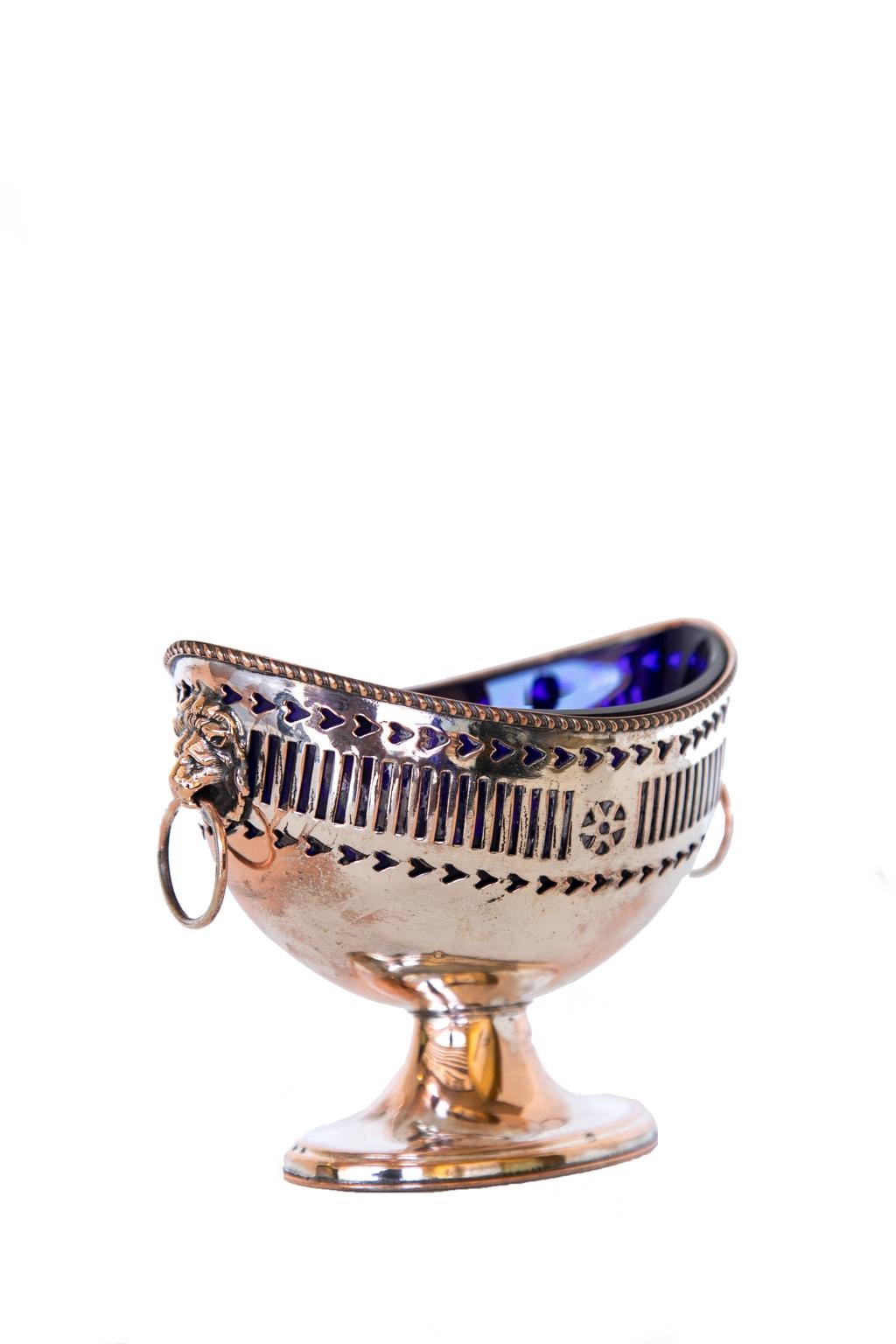 English Sheffield Master salt cellar, with the outer shell having a reticulated body with lion head pull handles. The liner is hand blown cobalt blue. The silver has some worn areas.
 
