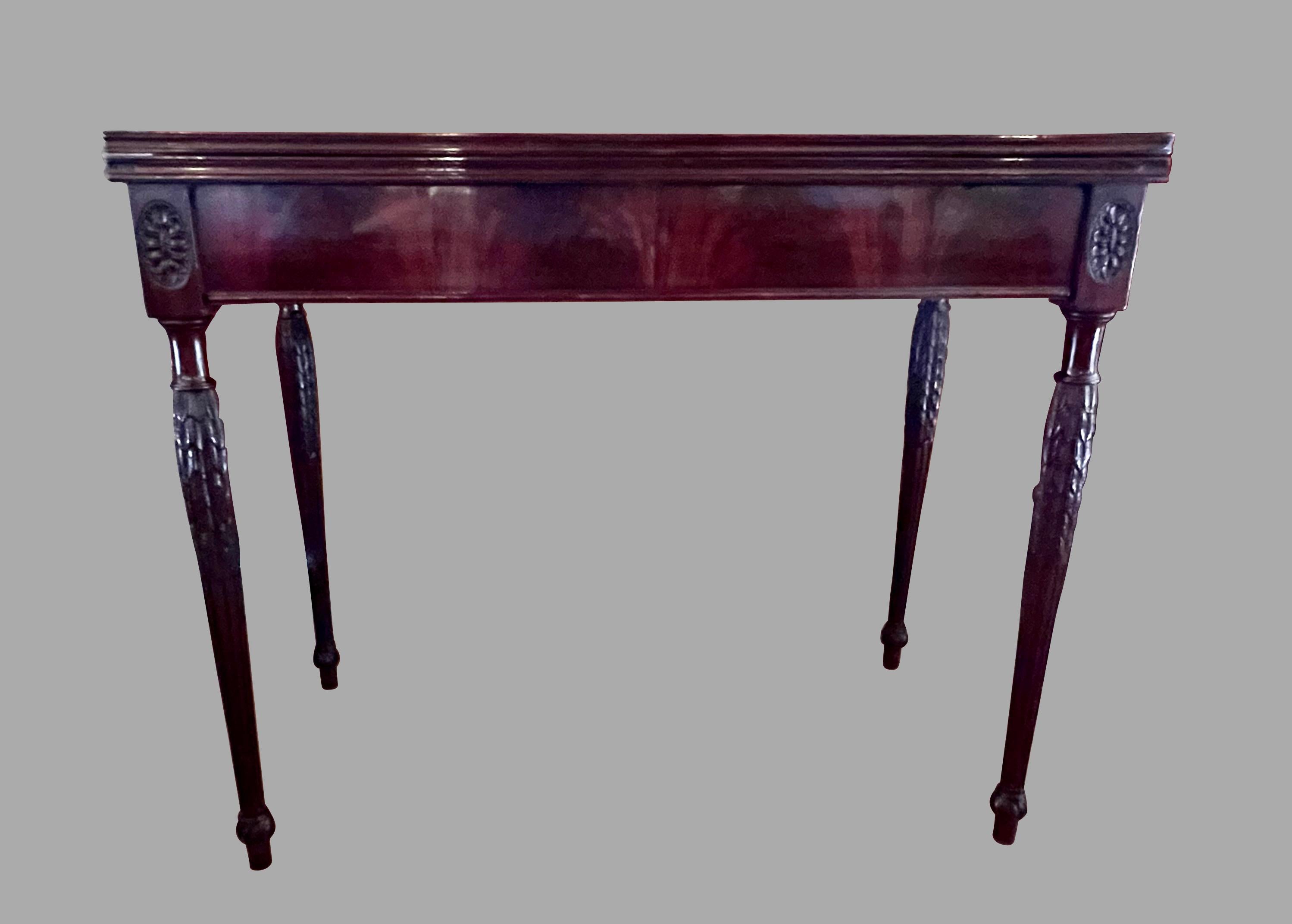 An eighteenth century Sheraton period English mahogany flip top games table, the richly figured deep brown French polished top opens to reveal a gilt-tooled brown leather surface supported by 2 swinging rear legs. The fluted and carved tapered legs