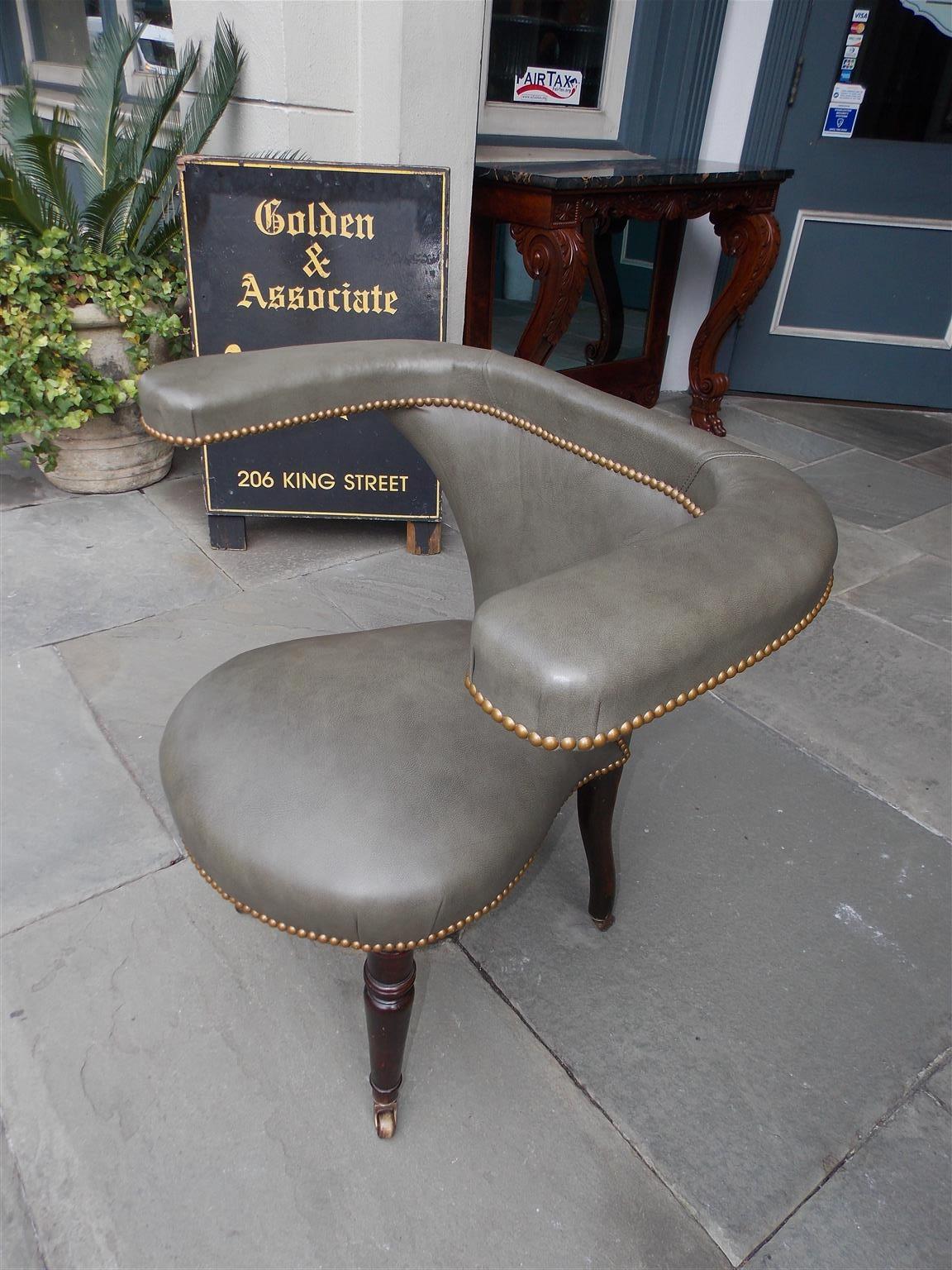 English Sheraton mahogany cock fighting chair with flanking curvature arms, brass tacked leather, and resting on turned bulbous ringed legs with the original brass casters. Early 19th century.