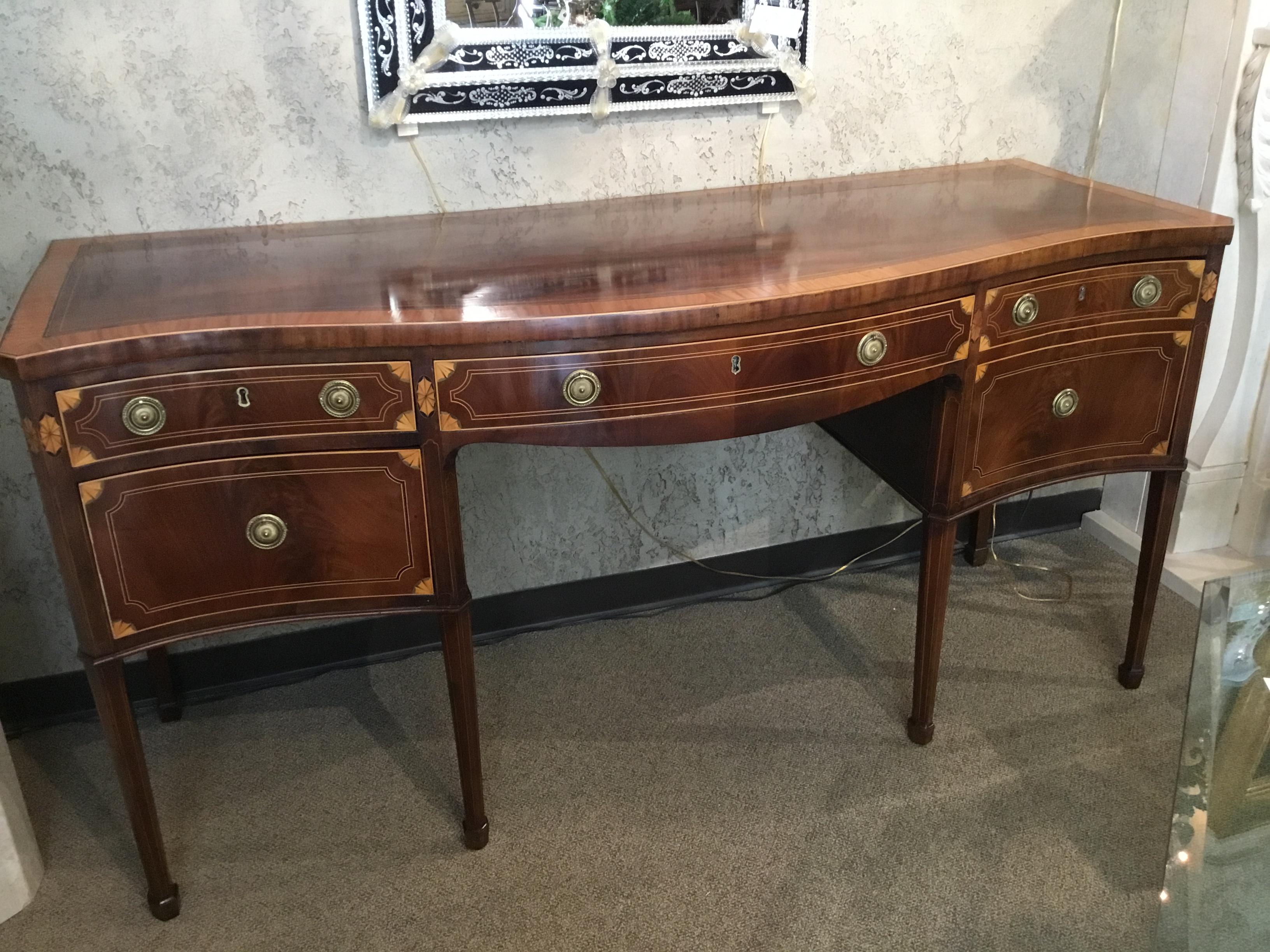 English, 19th century sideboard with fine marquetry inlay of satinwood and ebony. The flame mahogany
is lovely with the original finish and patina. The shape is of serpentine form with a graceful curve
to the center front. Three drawers under the