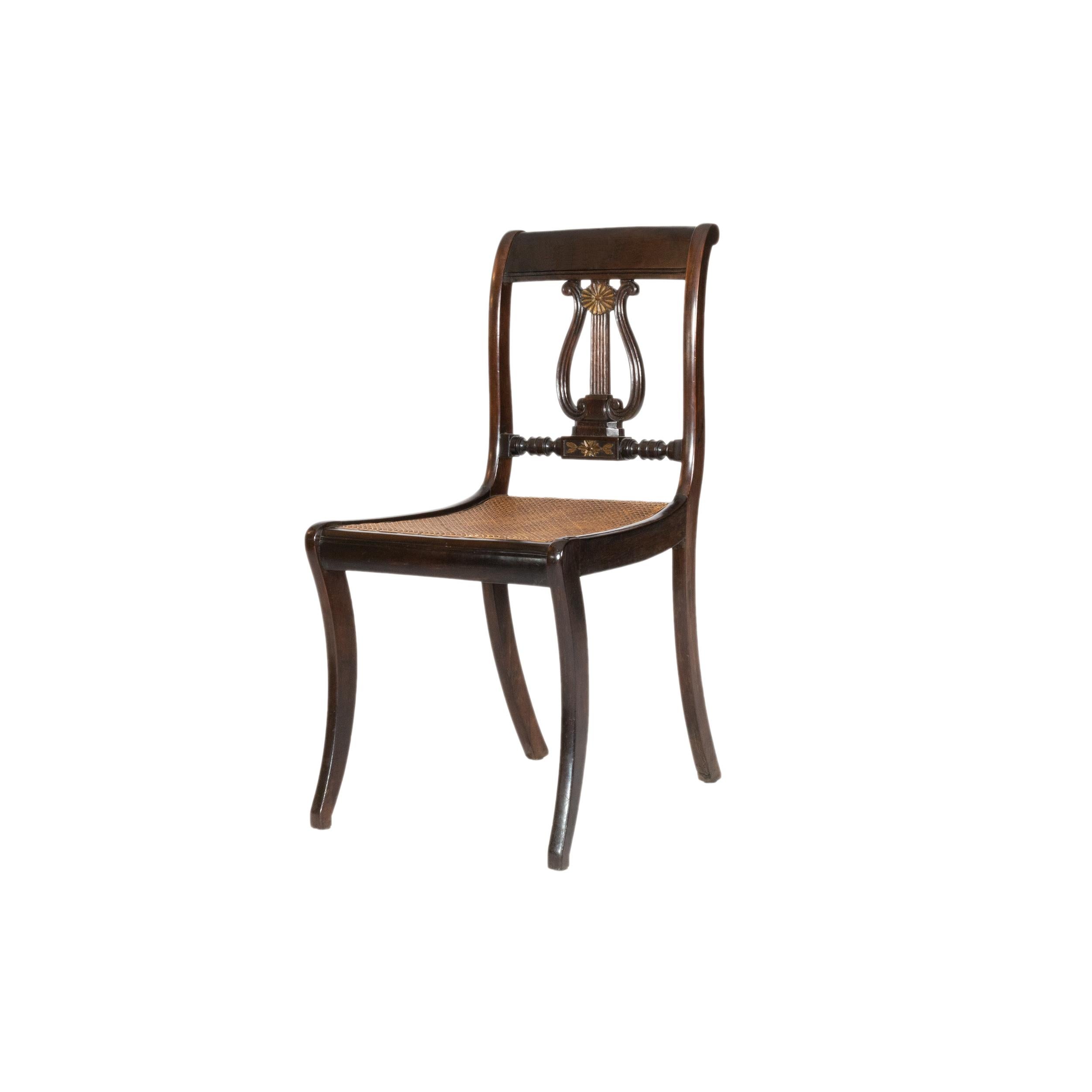 Una magnífica silla de comedor de estilo Sheraton con respaldo tallado en forma de lira musical inspirada en la mitología griega.
Asientos de paja natural intactos. Silla impecable - más disponibles.