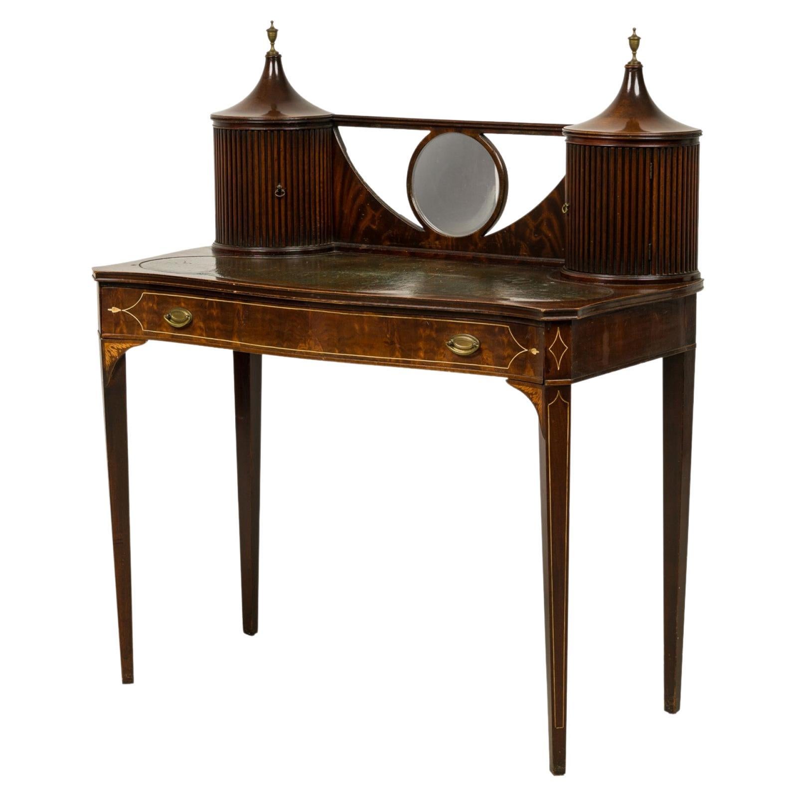 English Sheraton-style (19th century) mahogany vanity dressing desk with a central circular mirror mounted in a backrail between two cabinet compartments with rounded front fluted doors topped with urn finials, resting on a rectangular desktop with