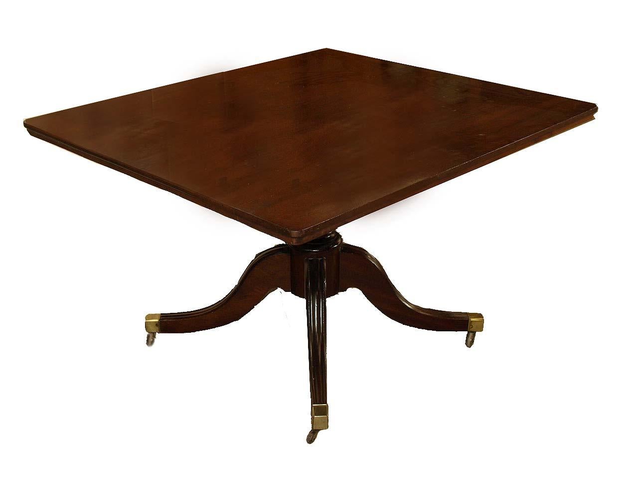 English Sheraton mahogany tilt top breakfast table, the top with beautiful grain supported by a band of mahogany underneath the perimeter; base with boldly turned shaft above the four legs with molded top edge, terminating with plain brass castors. 