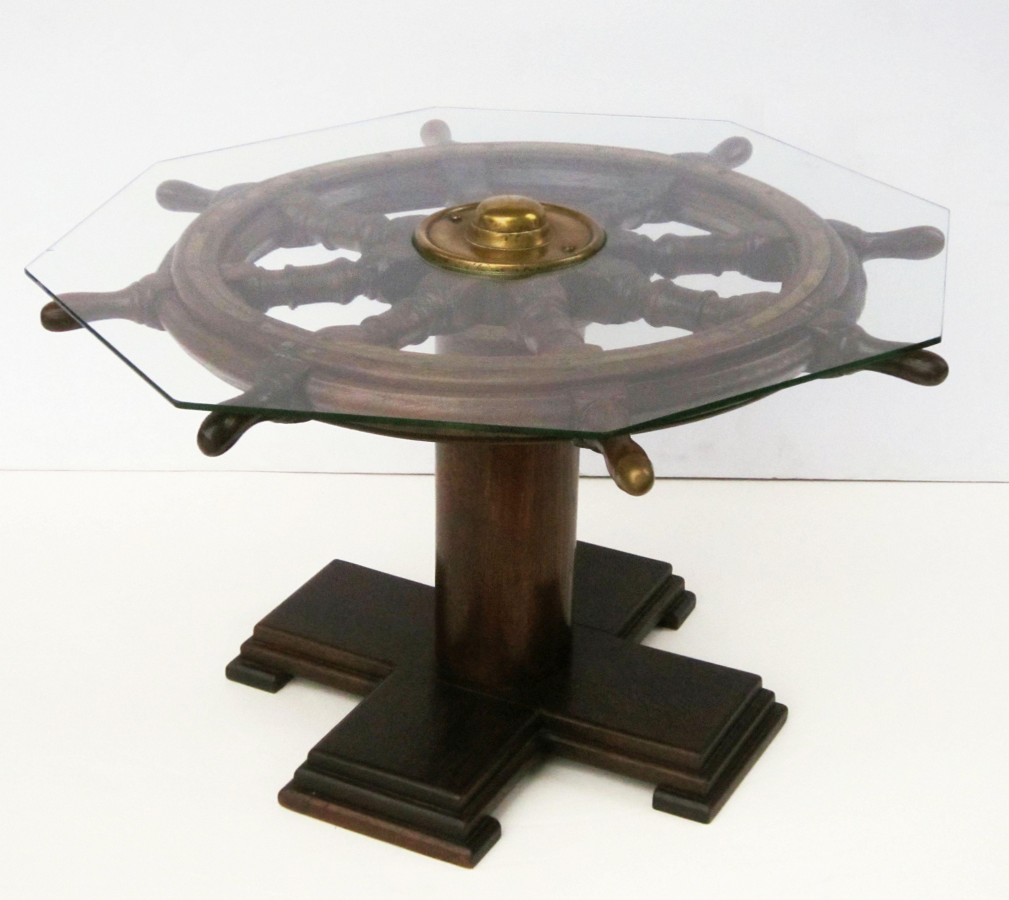 An English occasional or cocktail table fashioned from an authentic sailing ship's wheel of wood and brass, mounted to a wooden pedestal base, with removable eight-sided glass top.

Dimensions: Height 20 1/2 inches x width 36 inches x depth 36