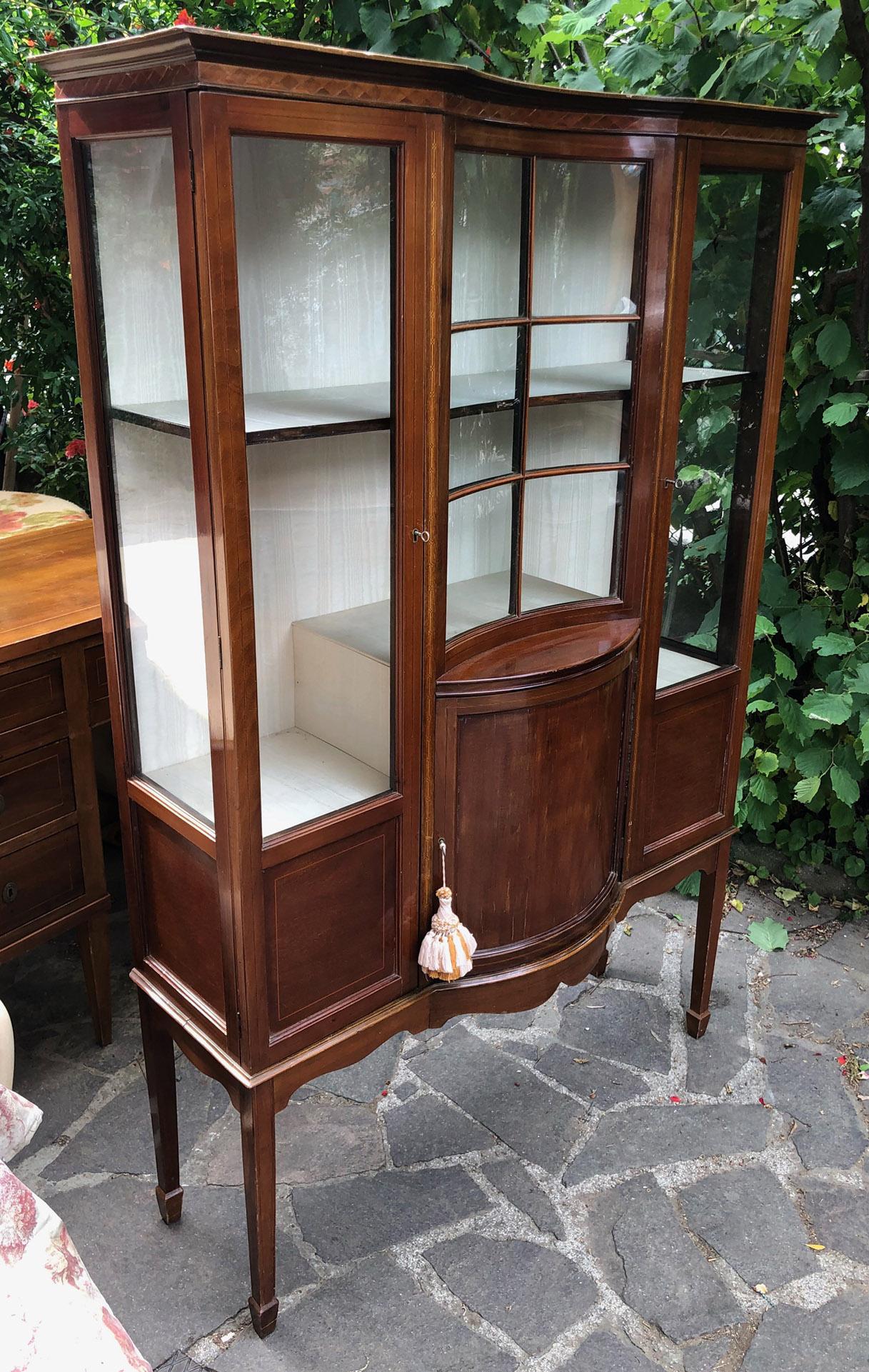 English showcase with three doors in mahogany, with glass on three sides. 
Curved central part.
Comes from an old house in the Florence area of Tuscany.
The paint is original in patina, honey amber color. 
As shown in the photographs and videos,
