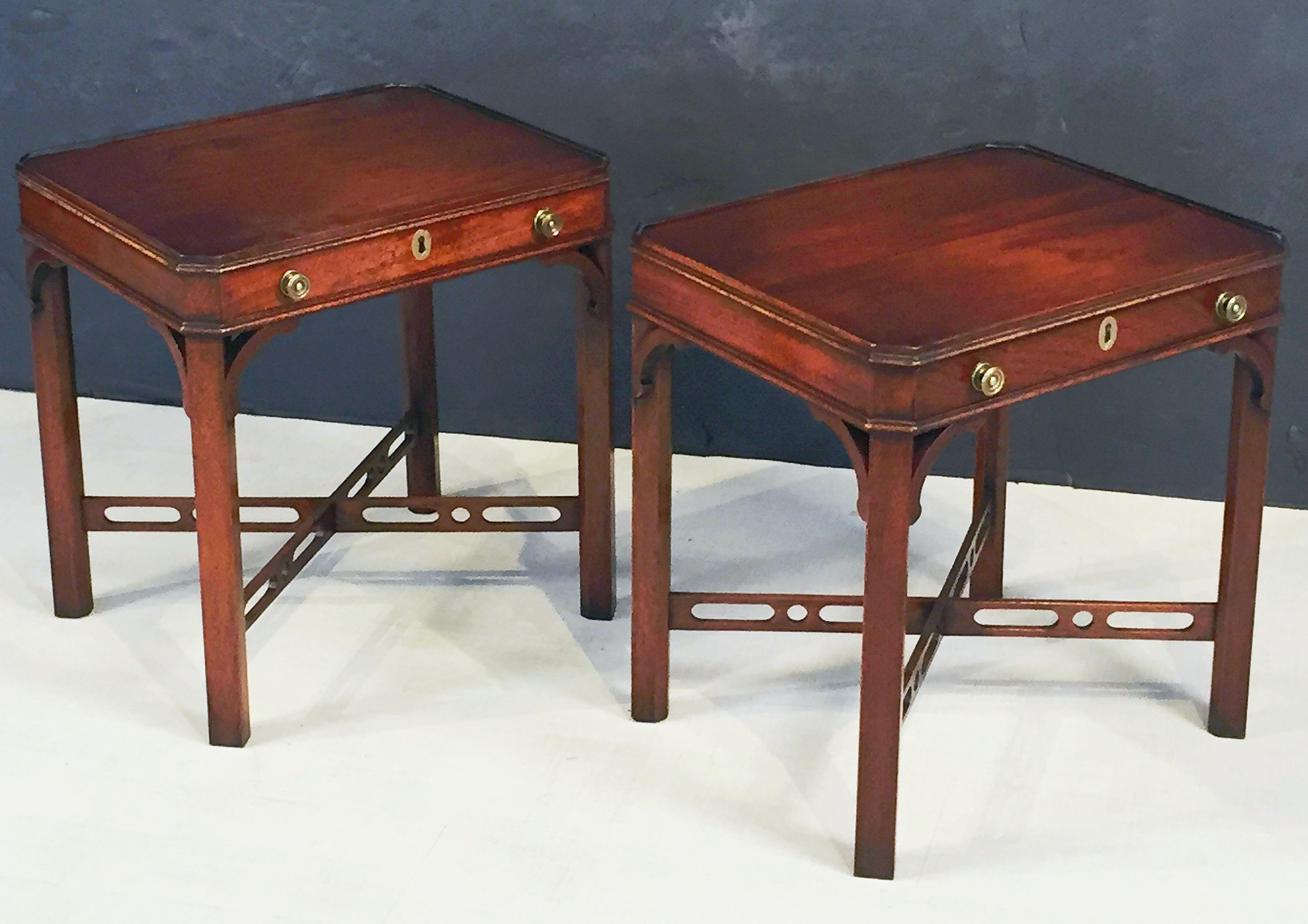 A fine pair of English side, occasional, or end tables of mahogany, in the Chippendale style - each table featuring a rectangular moulded top with canted corners, over a frieze with one long drawer and brass pulls and escutcheon, set upon canted