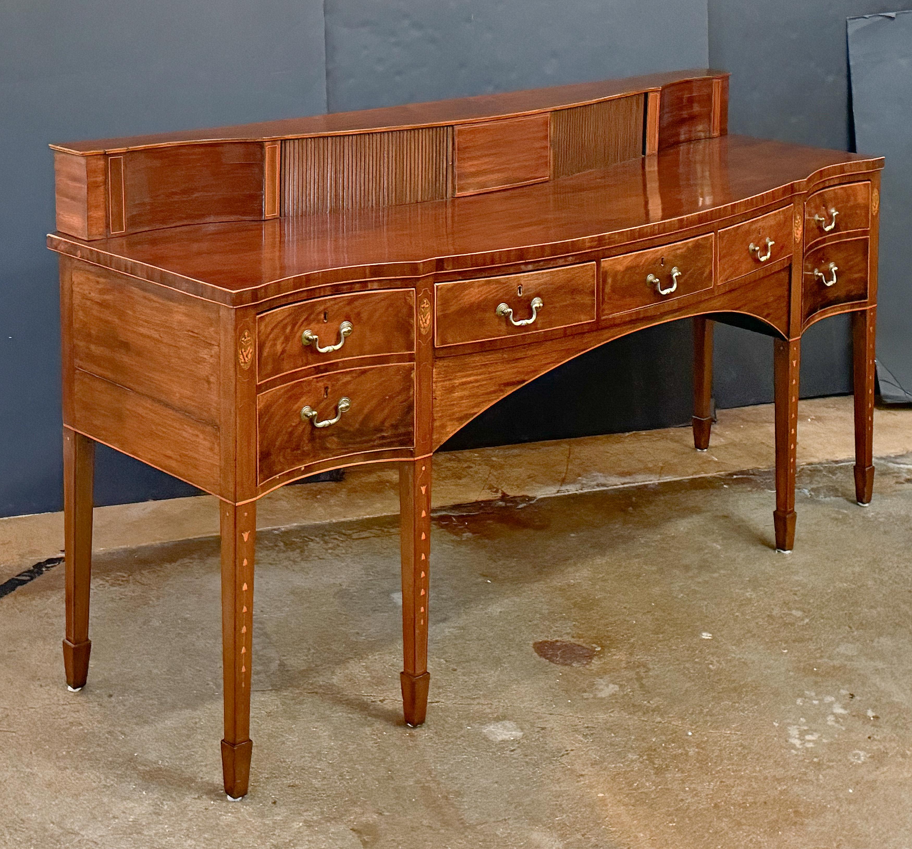 A handsome English sideboard server (or serving console) from the Georgian era - featuring a serpentine moulded top with raised gallery back - enclosing two compartments with tambour slides, over an inlaid mahogany frieze with opposing left-facing