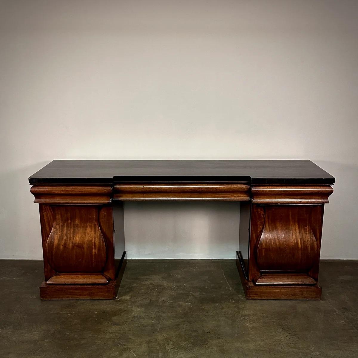 Elegante e funzionale credenza architettonica inglese del XIX secolo in mogano con piano nero ebanizzato. Il fregio superiore nasconde dei cassetti al di sopra di armadi laterali con piedistallo e scaffali interni a scomparsa. Il mogano ha una