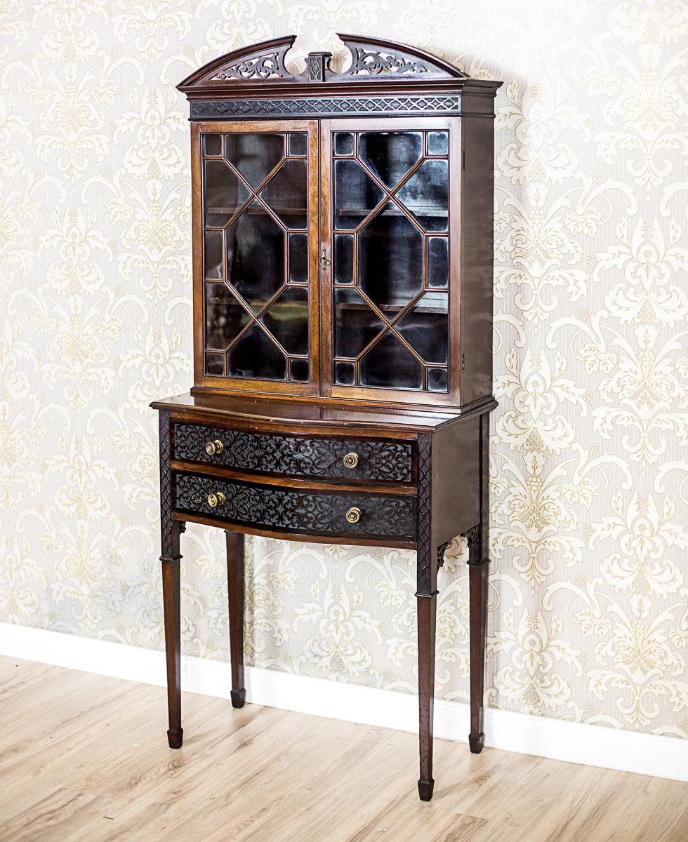 This cabinet is dated 1919; with the signature of a London manufactory, C. Williams.
Presented piece of furniture is of a lightweight construction, and is composed of a two-drawer base on high, straight legs and a glazed extension. The glazed parts
