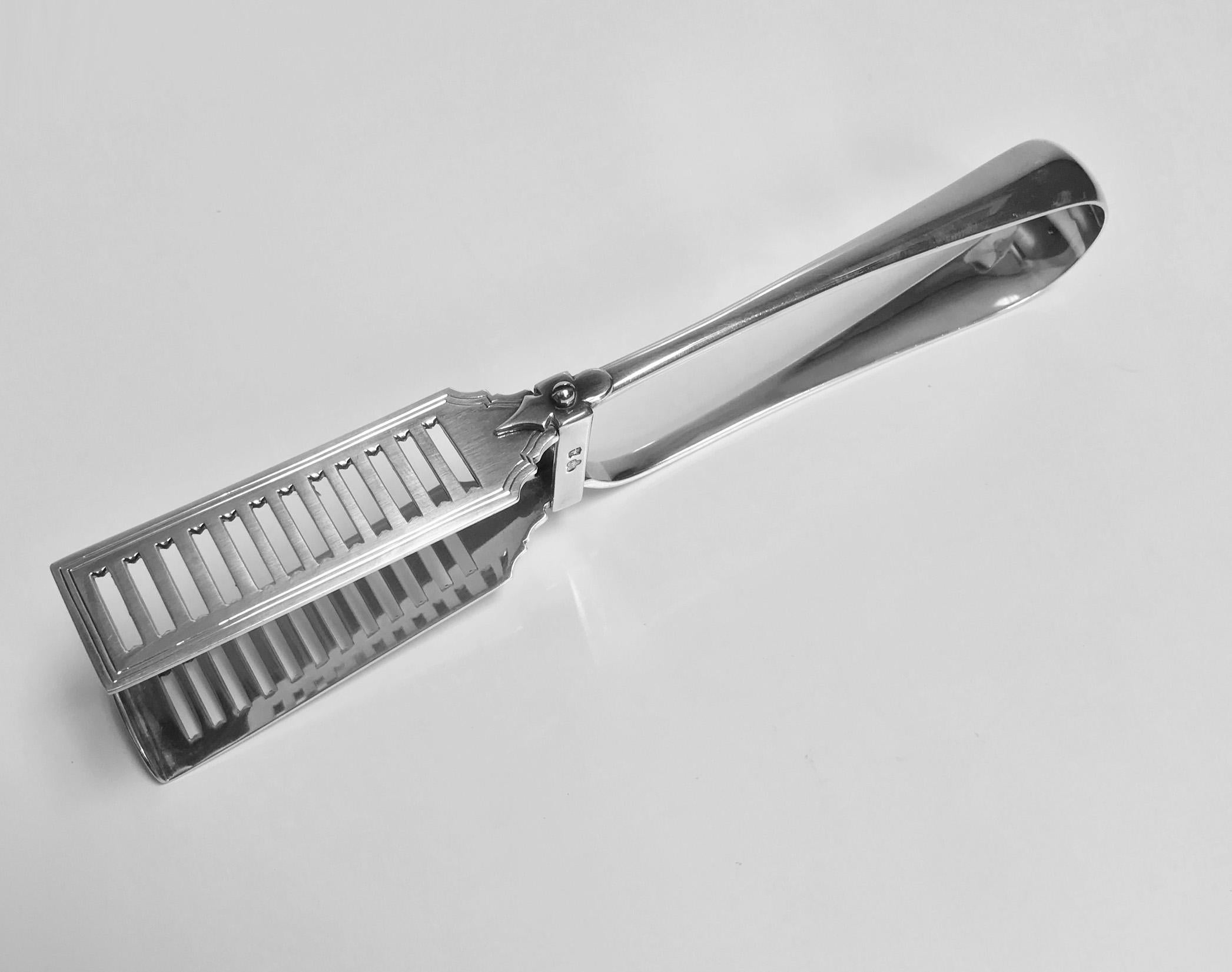 English silver asparagus tongs Goldsmiths Silversmiths Co. 1928. Plain Georgian style, pierced tongs, handle crested with hand grasping a book. Measures: Length 9 inches, weight 141.32 grams.